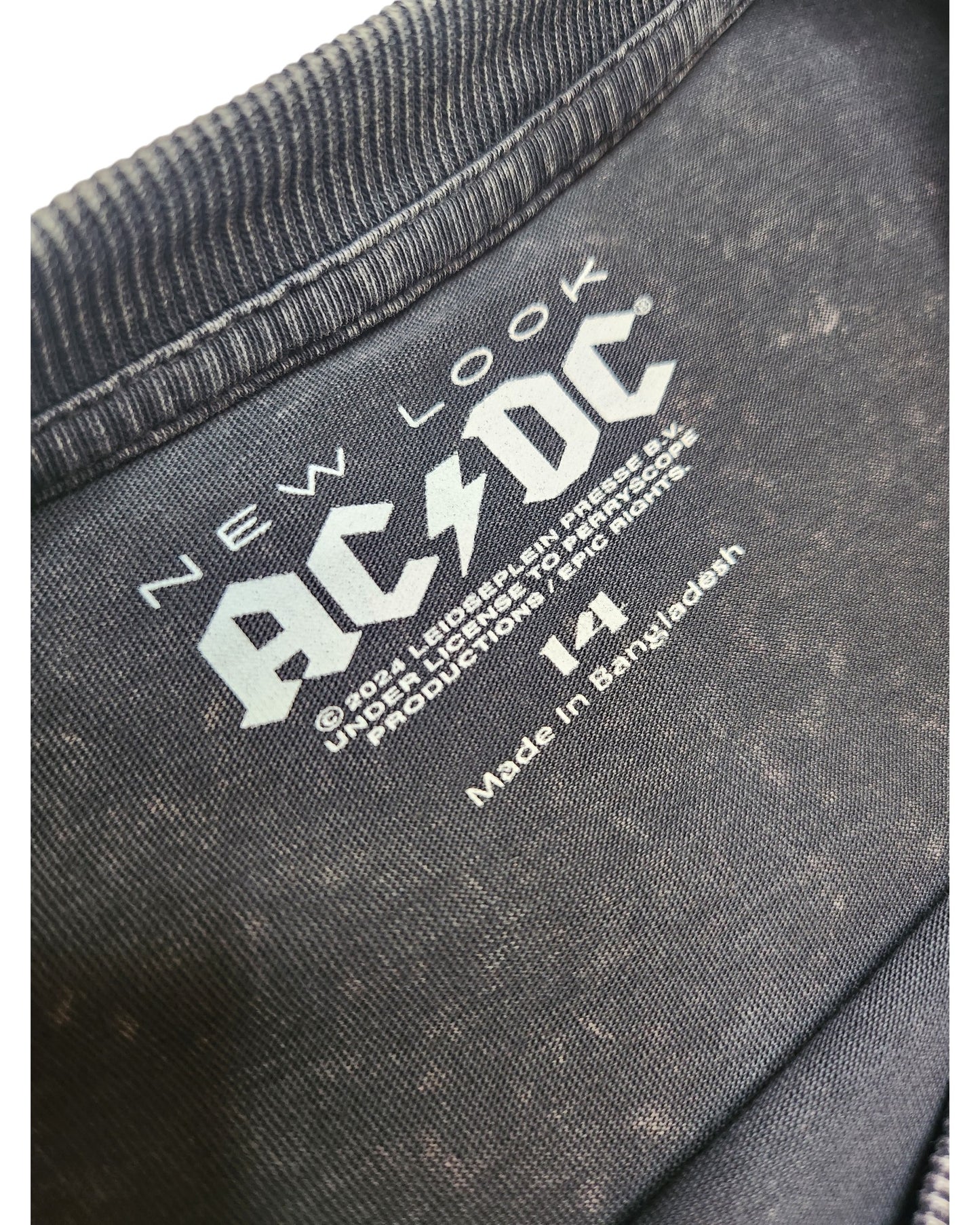 Close-up of a black collar on the Upcycled Breastfeeding & Pumping AC/DC Diamante Band t-shirt by New Look (UK14), showing the white printed label with size, licensing info, and Made in Bangladesh details—highlighting eco-friendly fashion.