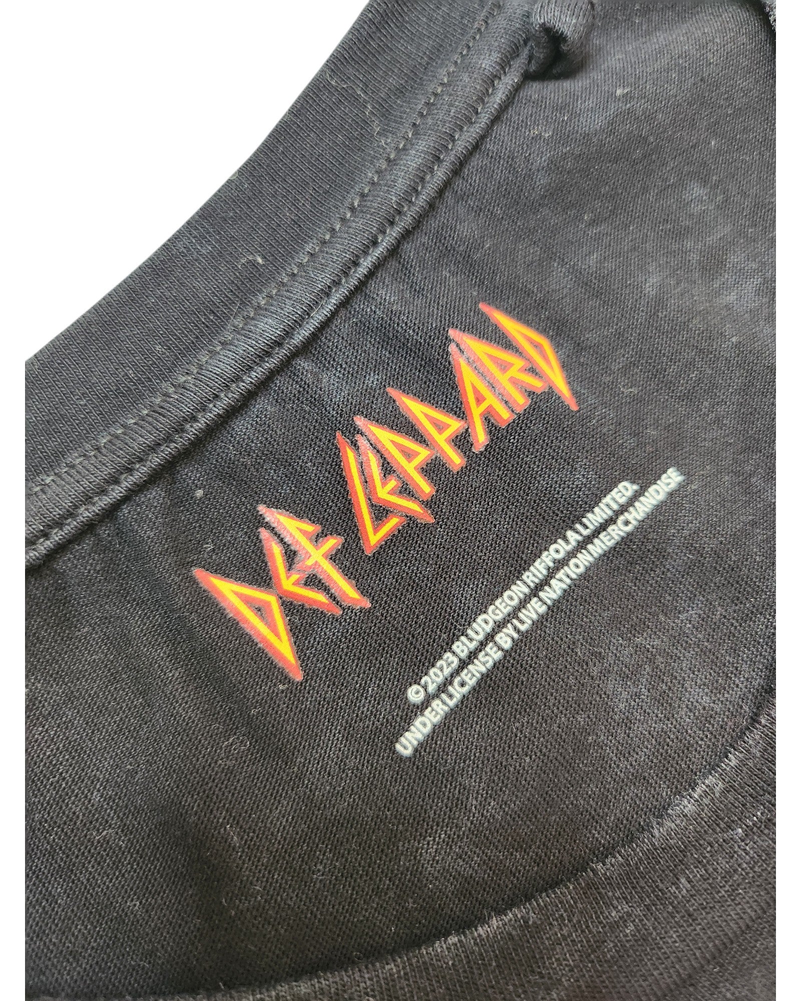 Close-up of the black Upcycled Breastfeeding & Pumping Def Leppard Band t-shirt (L) by Def Leppard, featuring the band logo in red and yellow on the collar with white copyright text below. Made from eco-friendly, upcycled materials for sustainable style.