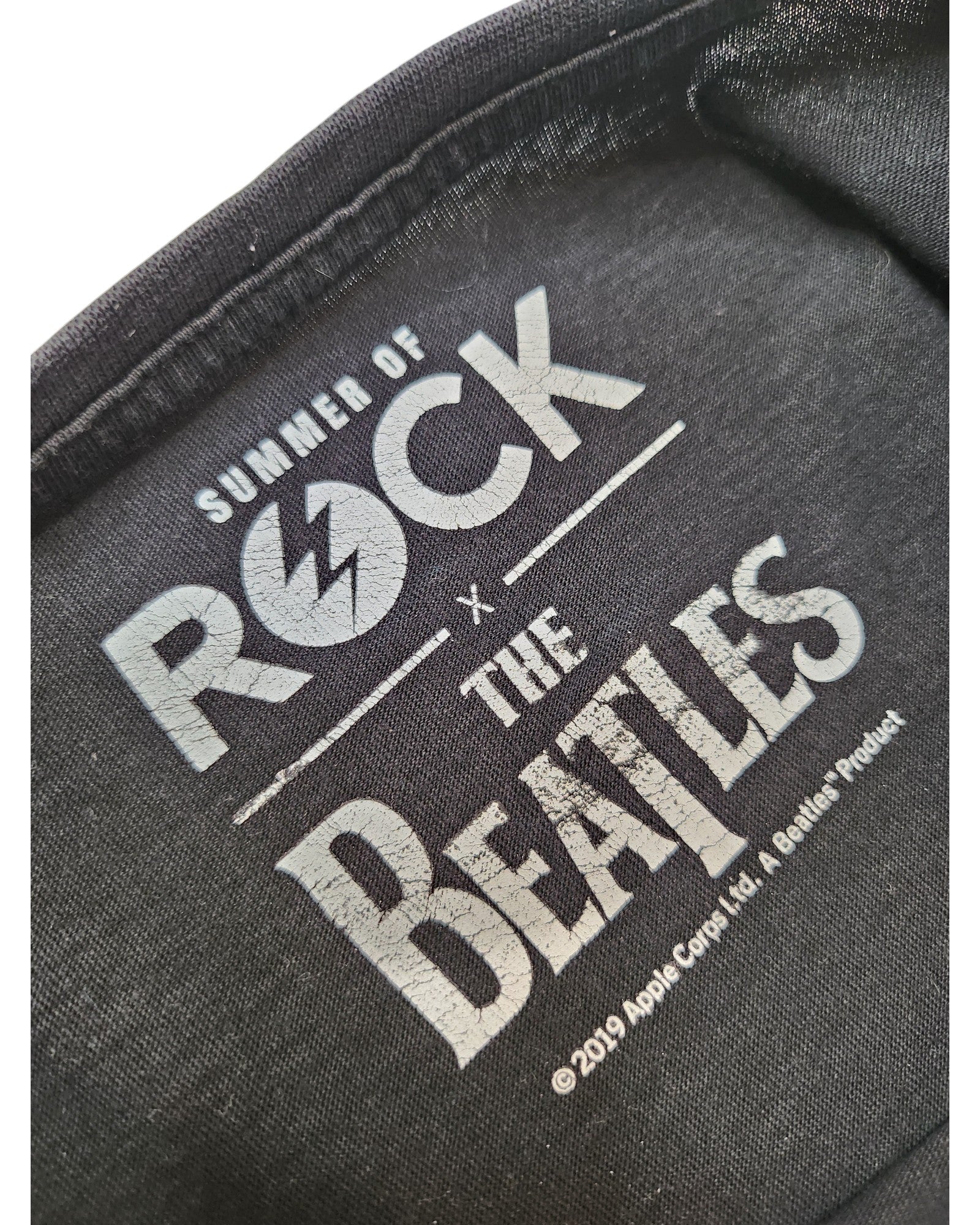 Close-up of a label on the Summer of Rock Upcycled Breastfeeding & Pumping The Beatles t-shirt UK10, featuring white text and celebrating eco-friendly fashion.