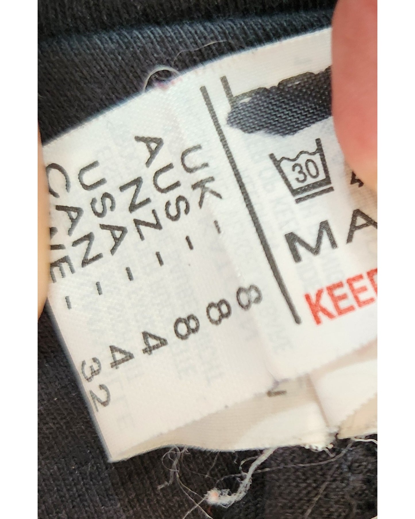 A close-up of a Boohoo label on an Upcycled Breastfeeding & Pumping Black The Rolling Stones Band t-shirt dress, UK8/US4. Label shows size info for UK, AUS, NZ, USA, and CAN, care symbols, and “KEEP.” Made from preloved clothing.