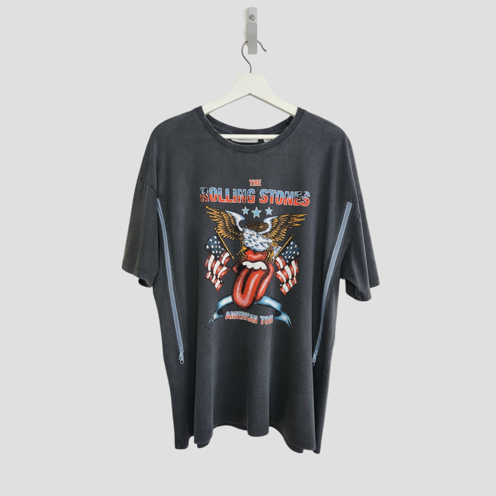 An upcycled black Rolling Stones US t-shirt (size L) by The Rolling Stones, designed for breastfeeding and pumping—features the band’s iconic graphics and “American Tour” on the front; displayed on a hanger against a white background.