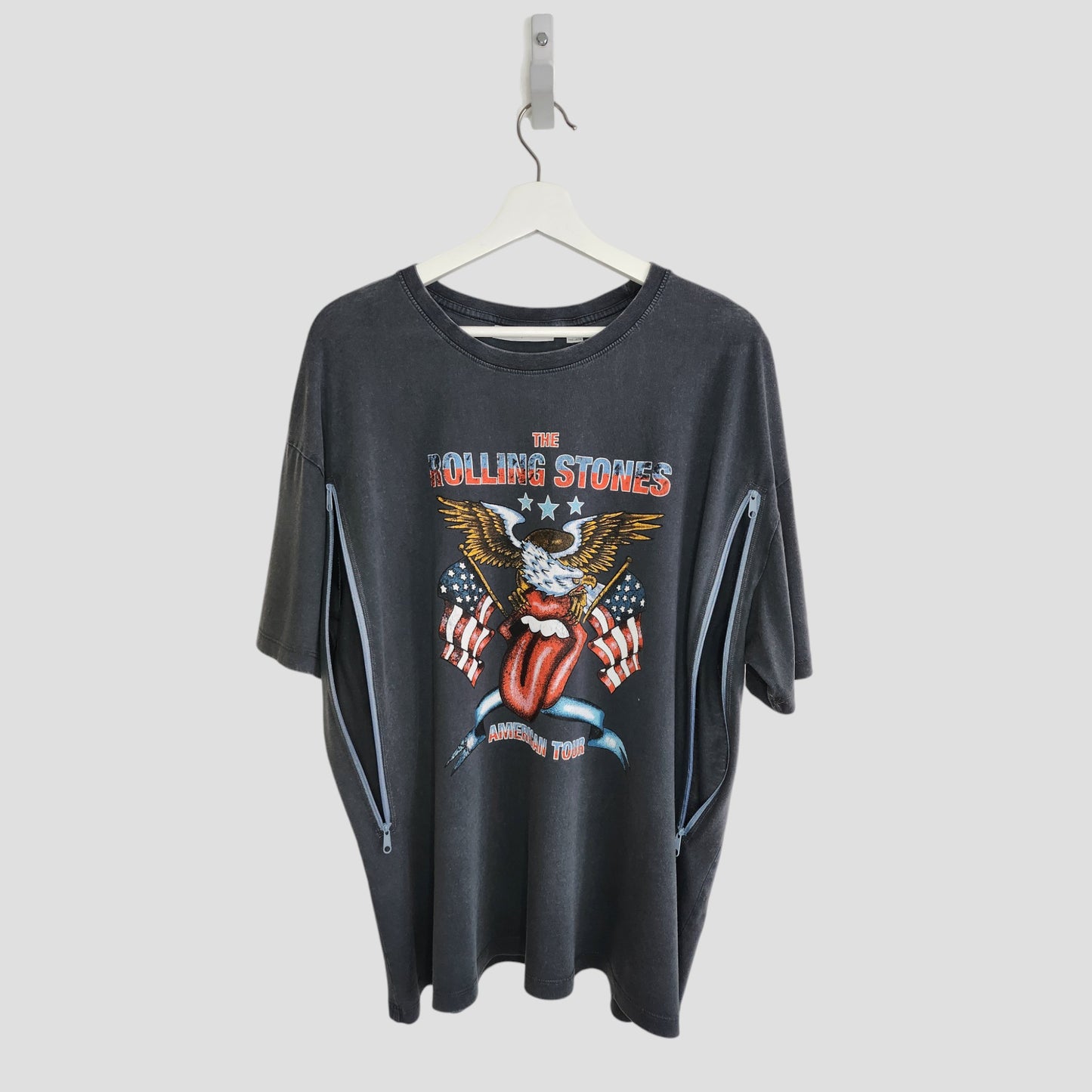 An upcycled Rolling Stones US t-shirt (L), black, featuring an eagle, stars, and the band’s tongue logo on the front. Two side zippers offer easy breastfeeding/pumping access. Preloved and hung on a white coat hanger.
