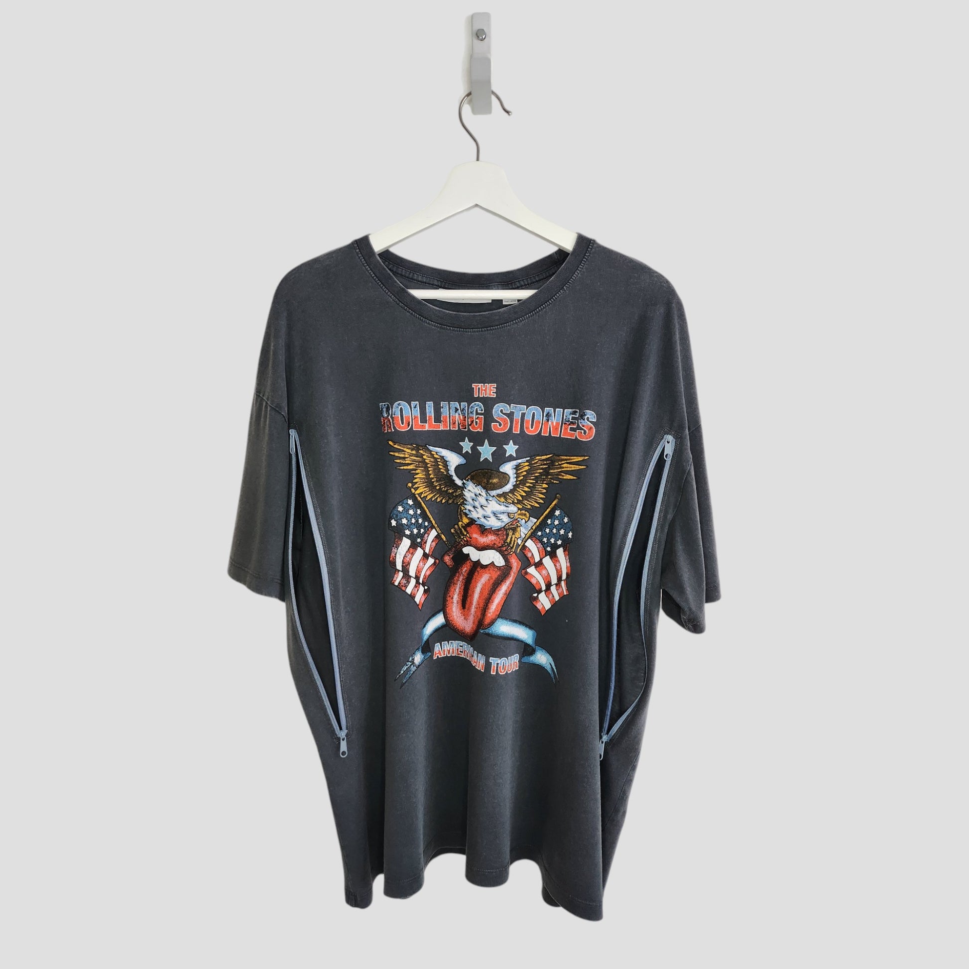 An upcycled Rolling Stones US t-shirt (L), black, featuring an eagle, stars, and the band’s tongue logo on the front. Two side zippers offer easy breastfeeding/pumping access. Preloved and hung on a white coat hanger.