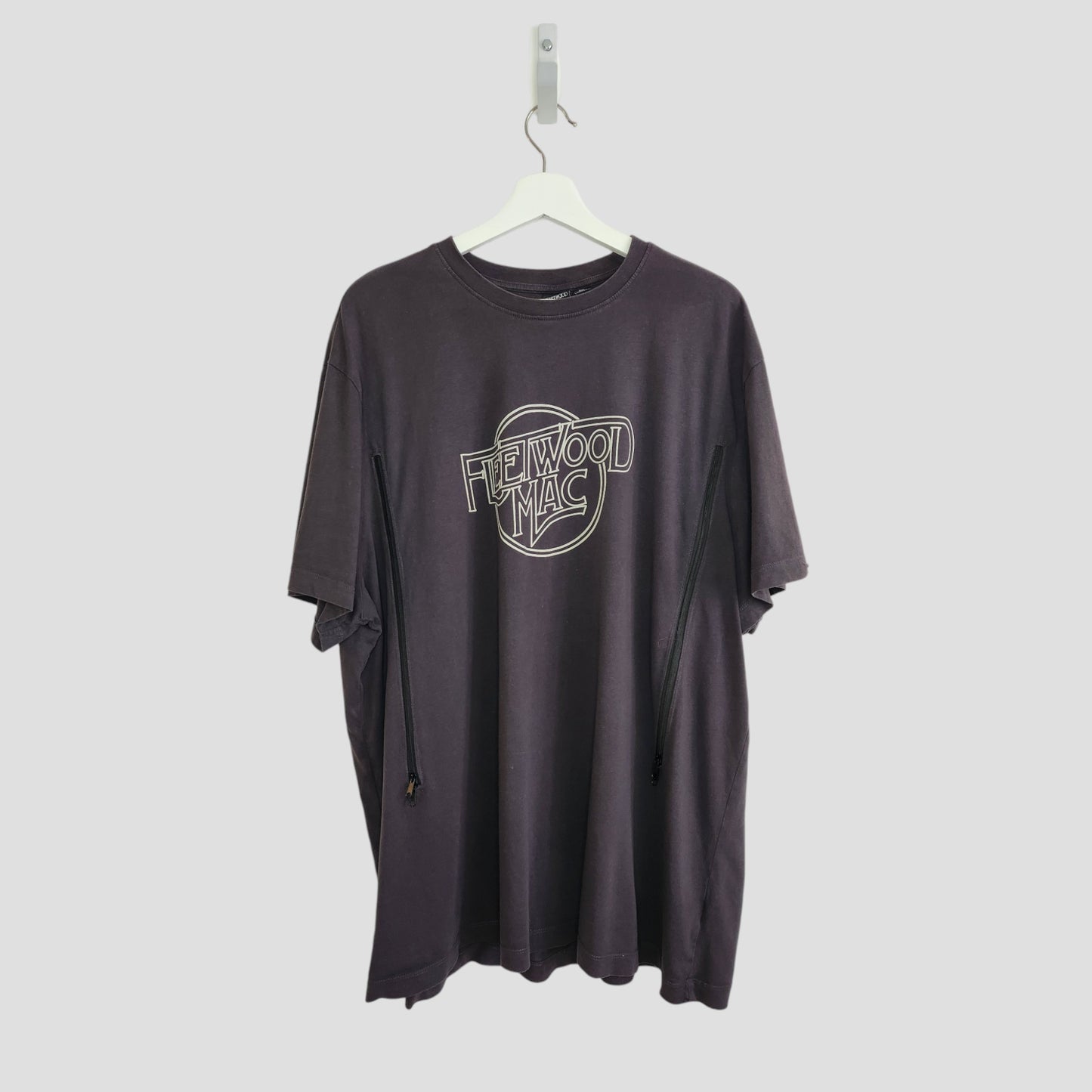 The Primark Upcycled Breastfeeding & Pumping Black/White Fleetwood Mac t-shirt 3XL, made from eco fashion materials, with a white outlined logo on the chest, hangs on a white hanger against a light gray background.
