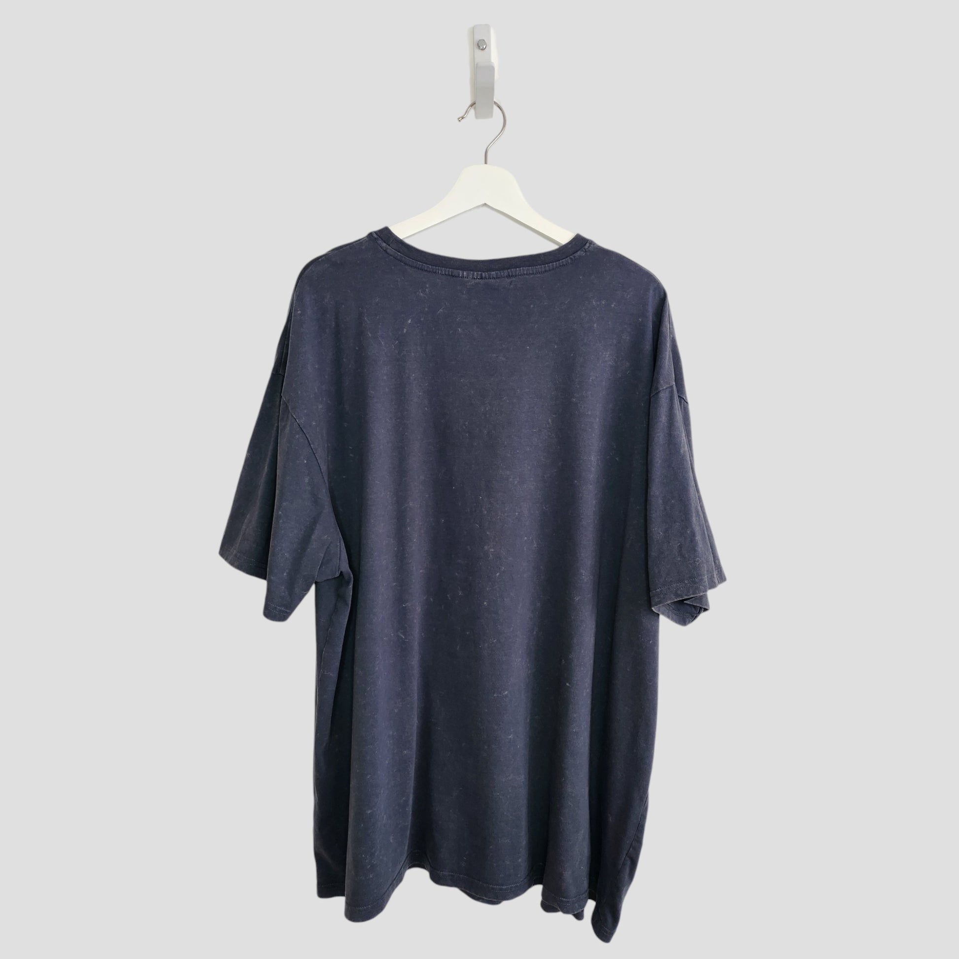 The Primark Upcycled Breastfeeding & Pumping Grey/Turquoise Nirvana Angel Band t-shirt (XL, UK18/20) made from eco-friendly materials hangs on a white hanger against a light gray background, shown from the back.