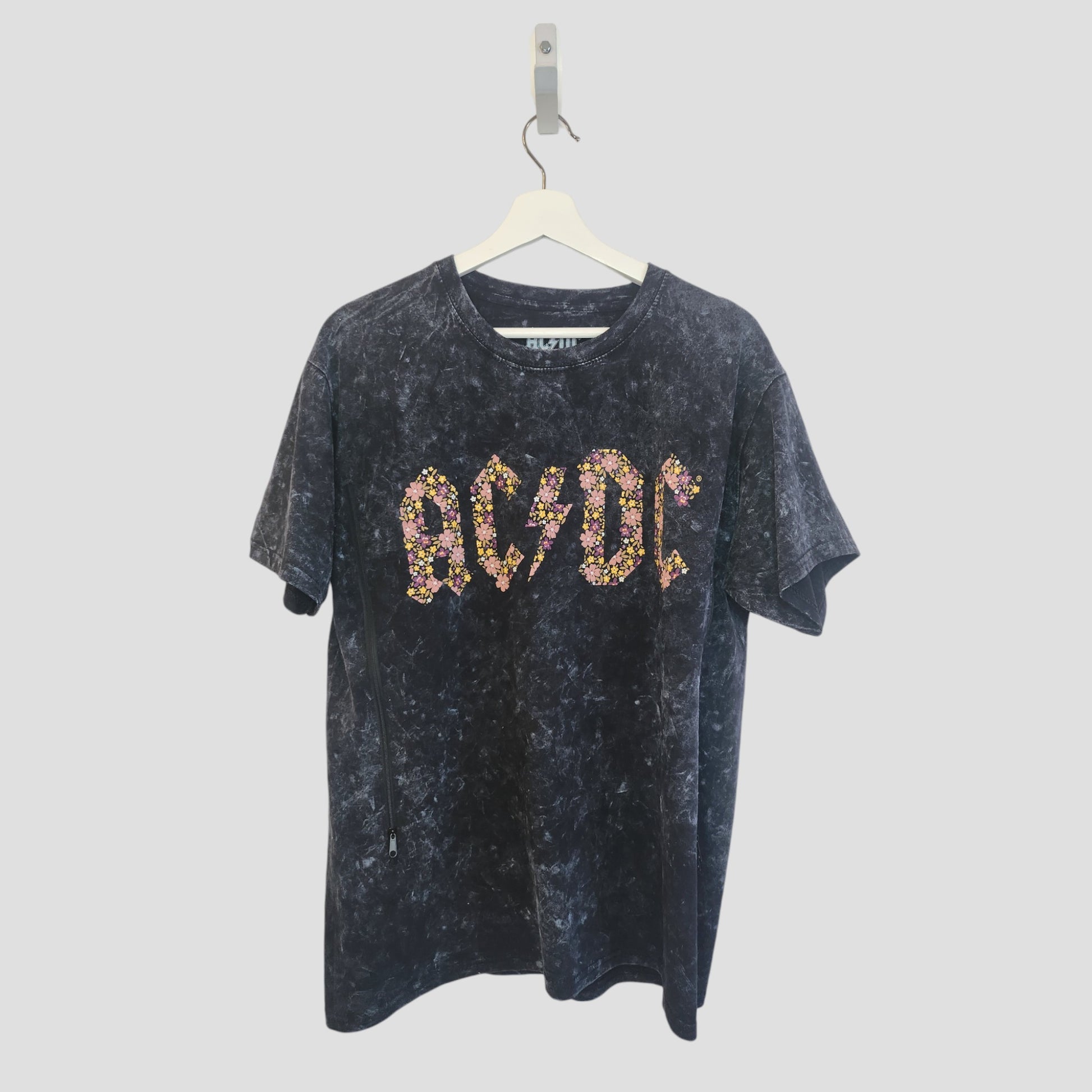 An upcycled black floral AC/DC band t-shirt (L) for breastfeeding and pumping hangs on a white hanger against a plain background, featuring the AC/DC logo in a colorful floral pattern.