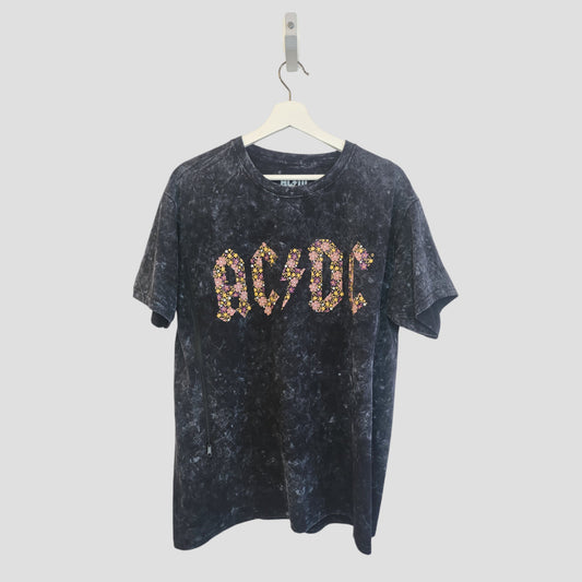 An upcycled black floral AC/DC band t-shirt (L) for breastfeeding and pumping hangs on a white hanger against a plain background, featuring the AC/DC logo in a colorful floral pattern.