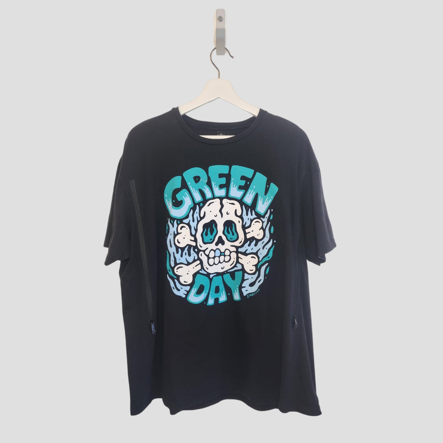 The Gildan Upcycled Breastfeeding & Pumping Black Skull Green Day Band T-shirt (XL, 100187) features a cartoon skull, blue flames, and bold GREEN DAY text in teal and white. It hangs on a white hanger against a plain background.