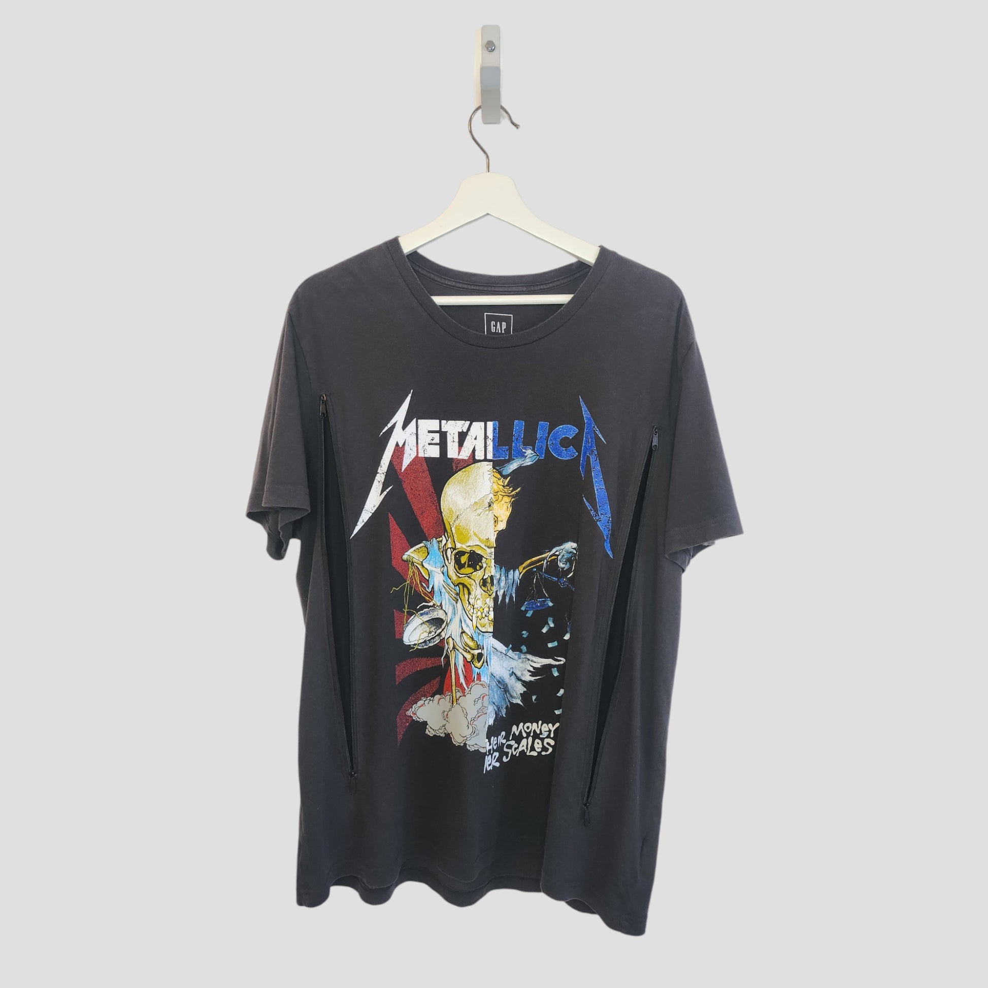 A black upcycled GAP Metallica band t-shirt (L) for nursing and pumping, featuring a colorful skull, lightning bolts, and Metallica ...And Money Be Sales, hangs on a white hanger—perfect for edgy breastfeeding fans.