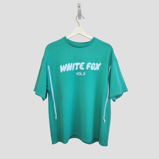 A green upcycled breastfeeding and pumping t-shirt (M, 100266) with WHITE FOX VOL. 3 in bold white letters on the front, two diagonal zippers on the sides, made from eco-friendly nursing top material, displayed on a hanger.