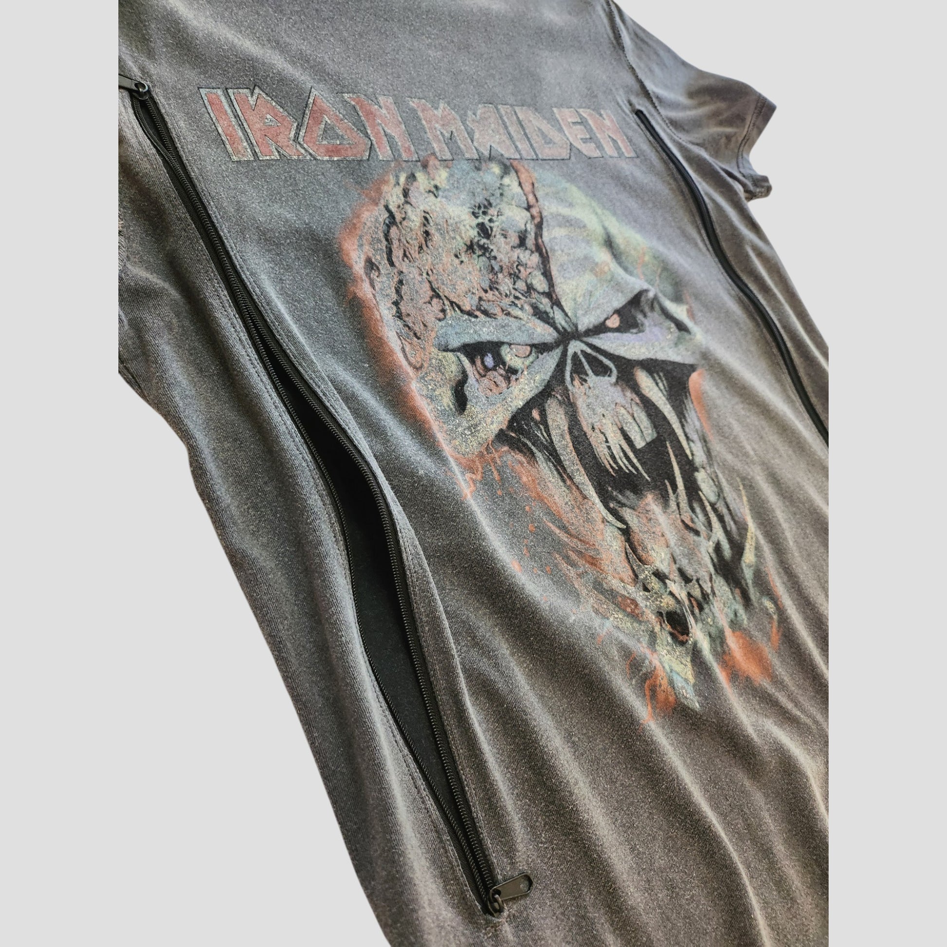 A close-up of a black Primark Iron Maiden t-shirt (UK10, 100234) with a menacing skull and red band logo graphic. This upcycled nursing top features two vertical zippers for breastfeeding or pumping access.