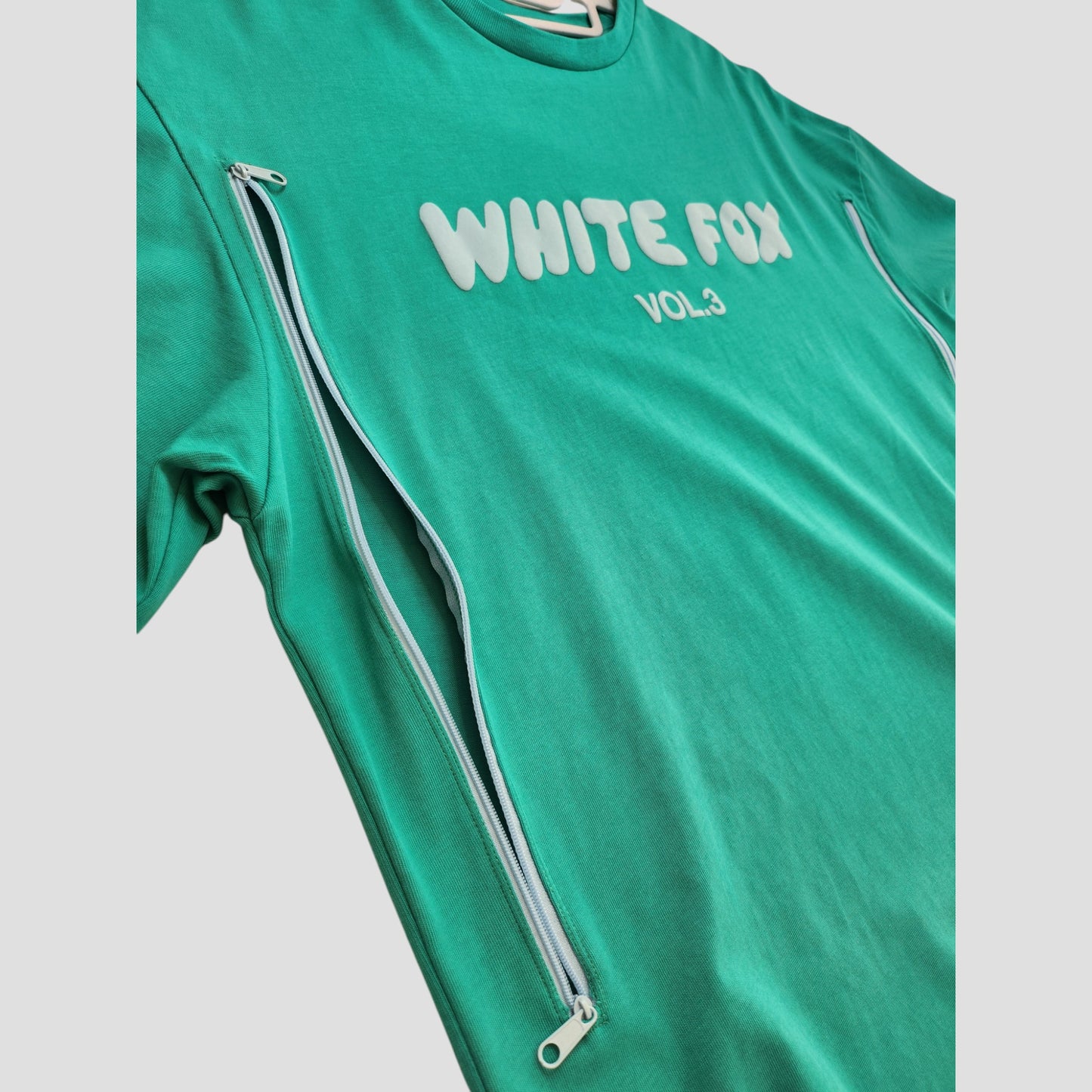 The Upcycled Breastfeeding & Pumping Green White Fox t-shirt (M) features WHITE FOX VOL.3 in raised white letters and diagonal side zippers for discreet nursing—an eco-friendly, modern solution for moms.