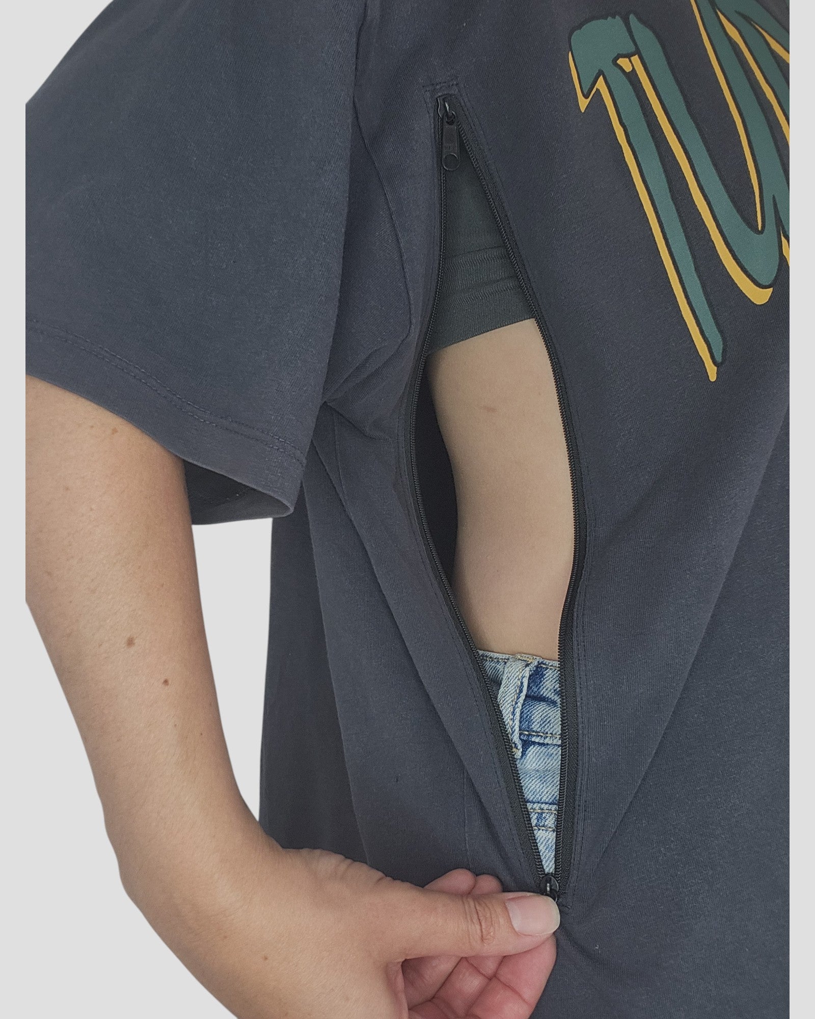 A person uses The Original Sew-On Zip Kit by touched out mama to add a side zipper to their black T-shirt for easy breastfeeding, revealing a hand in the pocket of light blue denim jeans.
