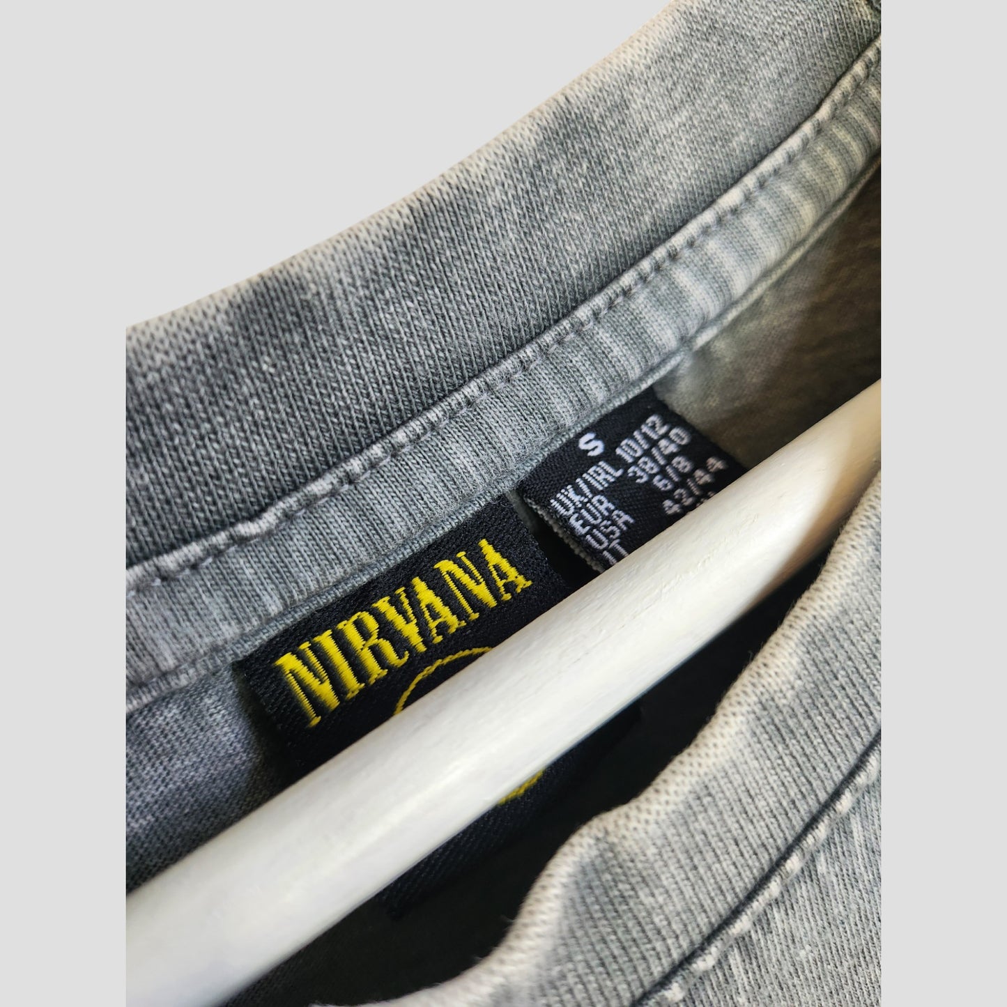 Close-up of an upcycled Primark Nirvana band oversized t-shirt dress in grey/pink, UK S (10/12), on a hanger showing the collar and label. Perfect affordable preloved find for nursing or pumping, with care and size tags behind the brand label.