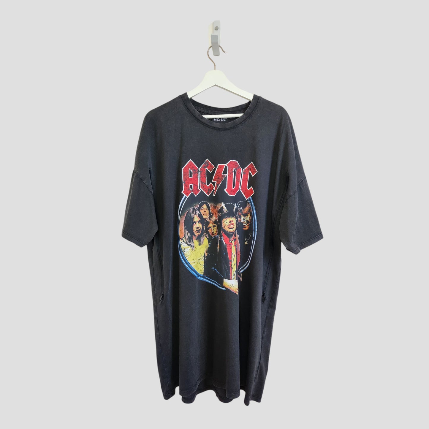 An upcycled Primark AC/DC Faces Band oversized t-shirt dress for breastfeeding and pumping, size L (100245), hangs on a white hanger against a plain light background.