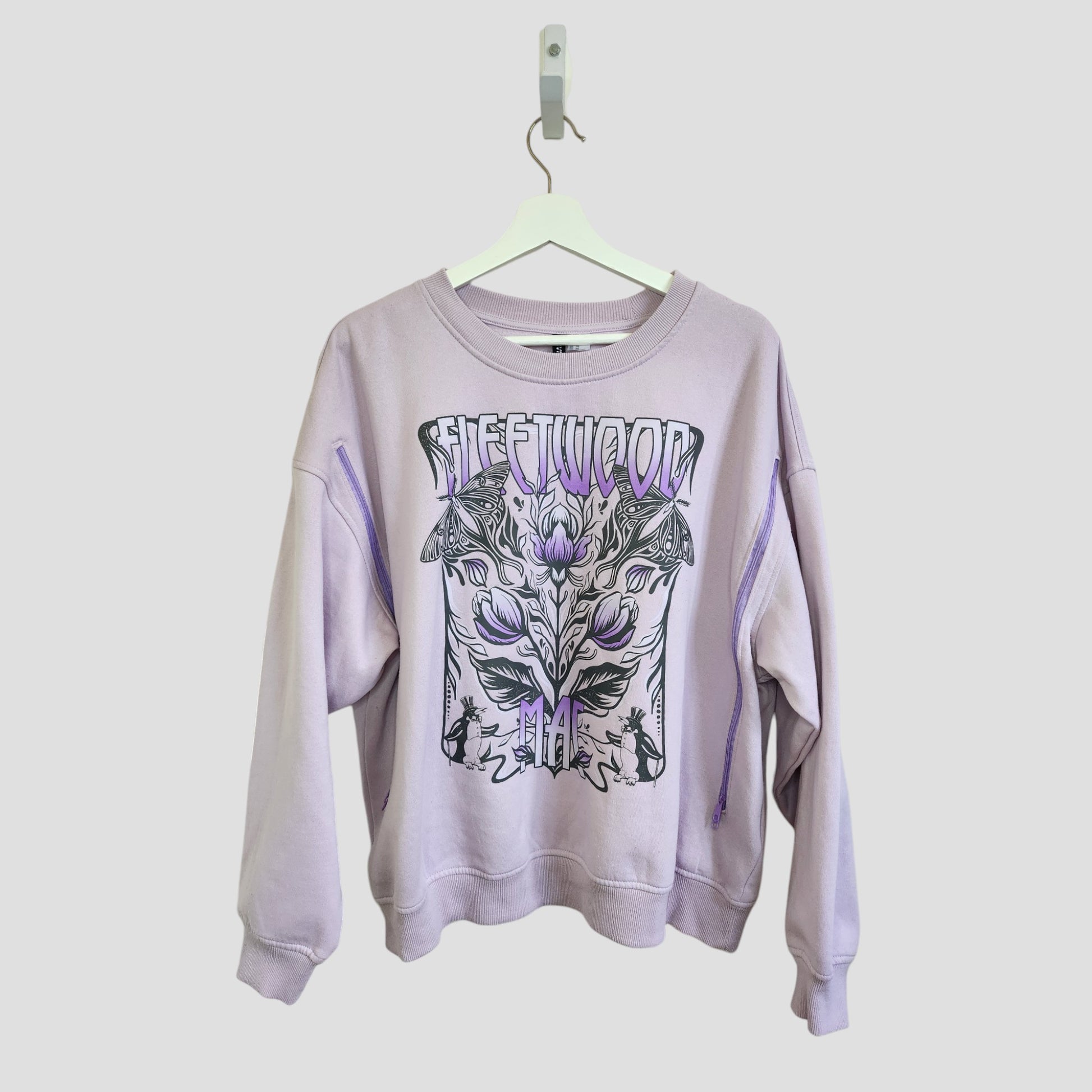 A lilac H&M Upcycled Breastfeeding & Pumping Fleetwood Mac Band Sweatshirt (XL) with black and lavender graphic and FLEETWOOD print, displayed on a white hanger against a plain background.