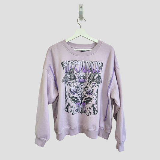 A lilac H&M Upcycled Breastfeeding & Pumping Fleetwood Mac Band Sweatshirt (XL) with black and lavender graphic and FLEETWOOD print, displayed on a white hanger against a plain background.