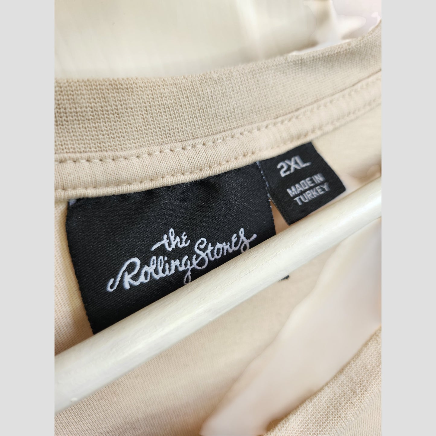A beige/red The Rolling Stones band t-shirt (2XL, Primark) is upcycled for breastfeeding and pumping convenience, featuring a close-up of its collar with a black tag. This sustainable piece (100305) hangs on a white hanger.