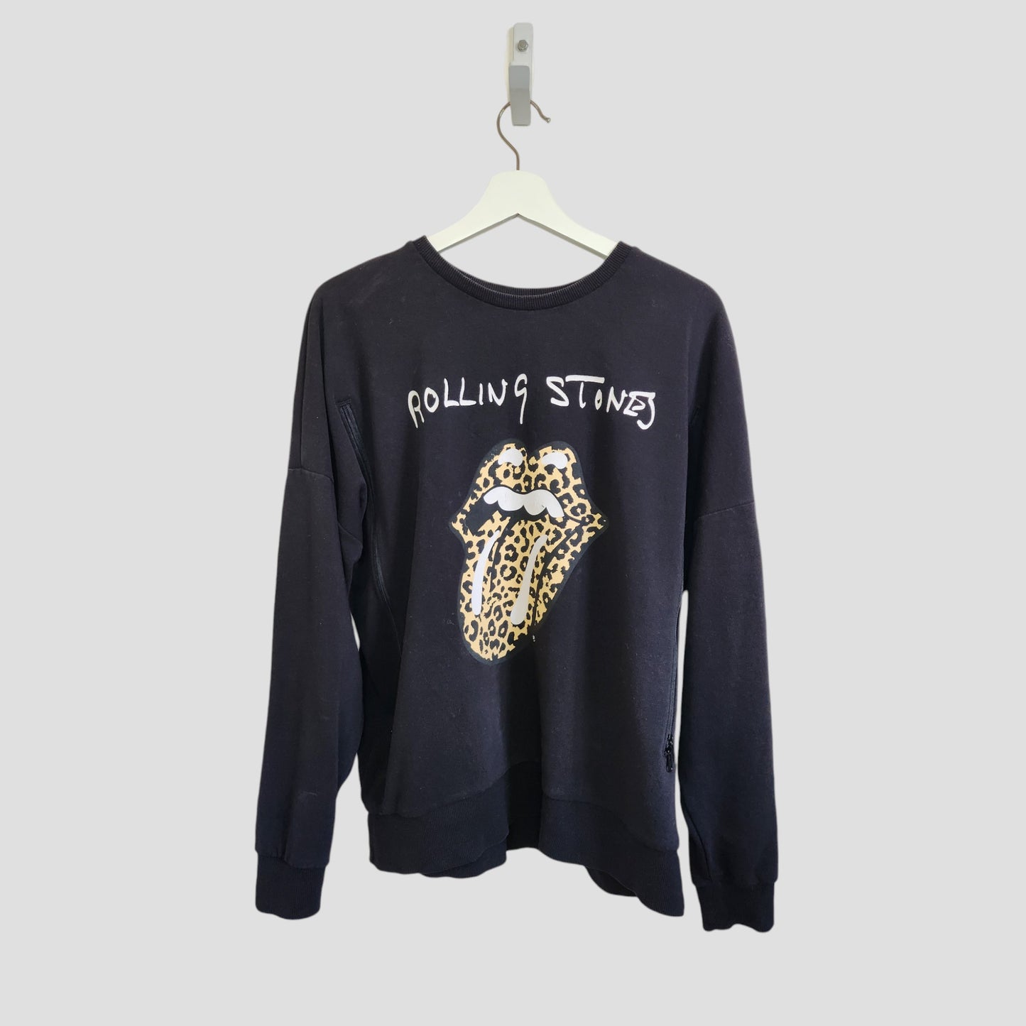 The Rolling Stones Upcycled Black/Leopard Band Sweatshirt (UK14, 100280) for breastfeeding and pumping, made from preloved clothing, features a leopard print tongue and lips graphic. Displayed on a white hanger against a light gray background.