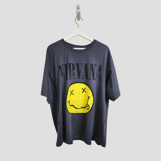 A grey upcycled Nirvana T-shirt by Primark (size XL, UK18/20) hangs on a white hanger. It features the band's name in bold black above a yellow smiley face graphic with crossed-out eyes and a wavy mouth. Great for breastfeeding & pumping.