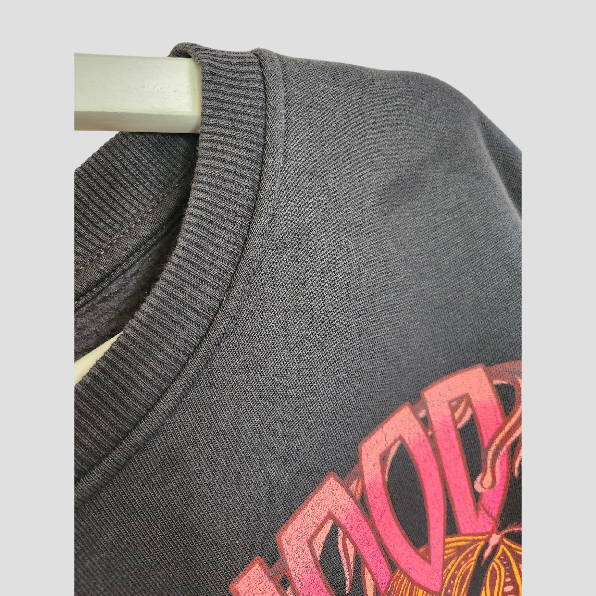 Close-up of a dark grey Primark crewneck sweatshirt (UK14/16) with a vibrant Fleetwood Mac floral band graphic—an upcycled breastfeeding and pumping top that combines eco-friendly style with nursing convenience.