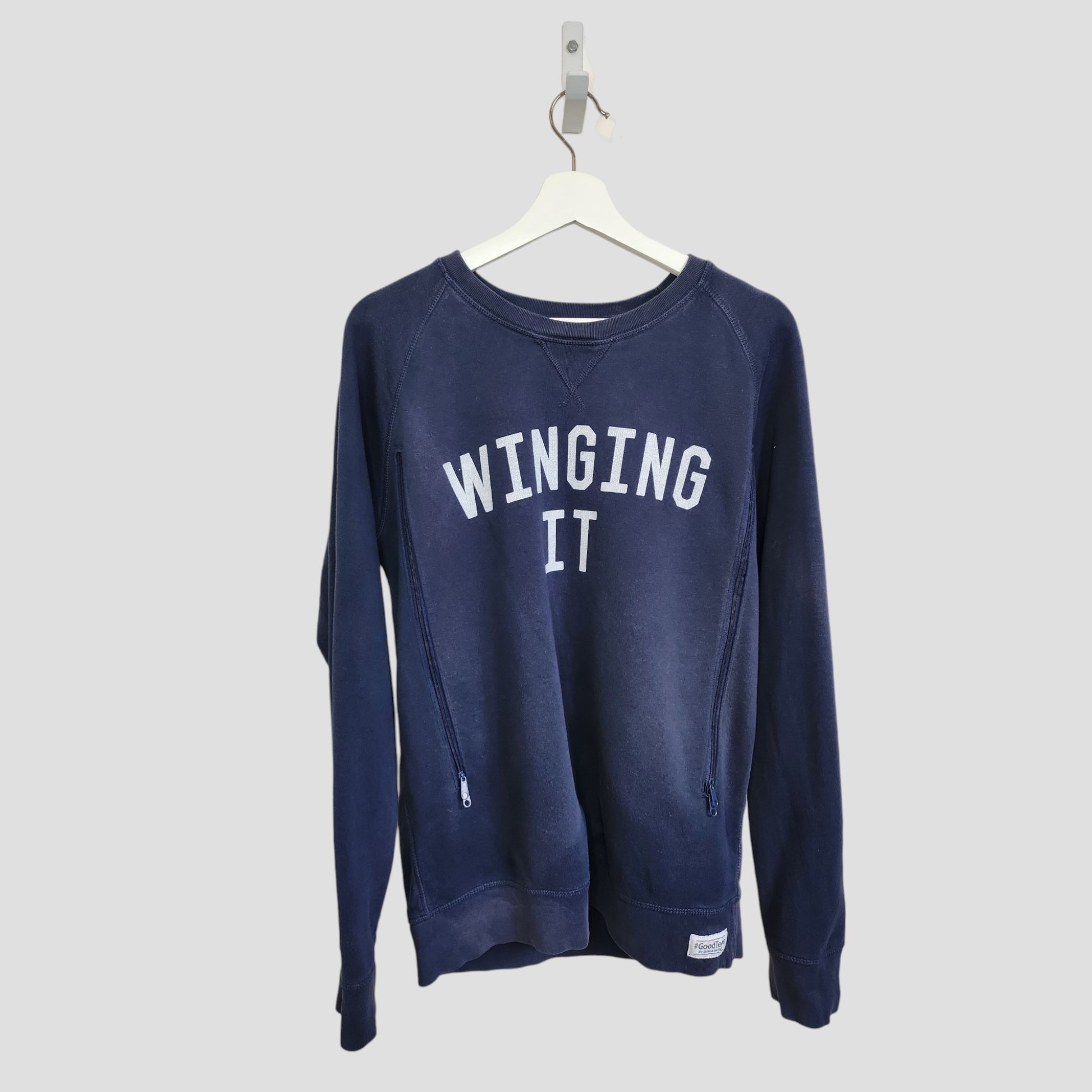 The Selfish Mother Upcycled Breastfeeding & Pumping Navy Blue Winging It Sweatshirt (L, 100099) with white text hangs on a white plastic hanger against a plain light gray background, making stylish and affordable maternity wear.