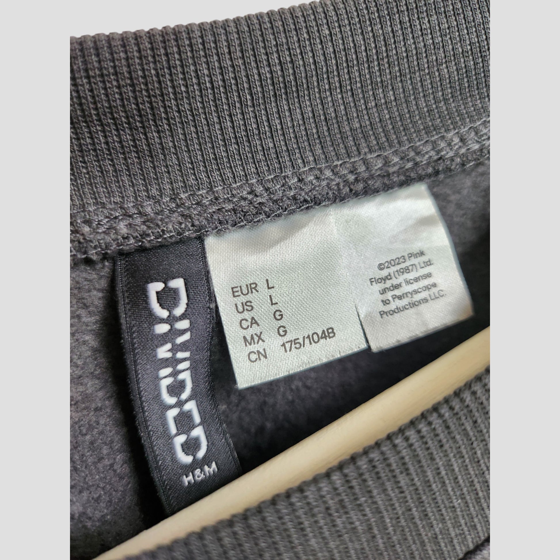 Close-up of a black H&M label and white size tag inside an upcycled preloved H&M Breastfeeding & Pumping Pink Floyd Band Sweatshirt L, showing multi-country sizes and washing instructions.