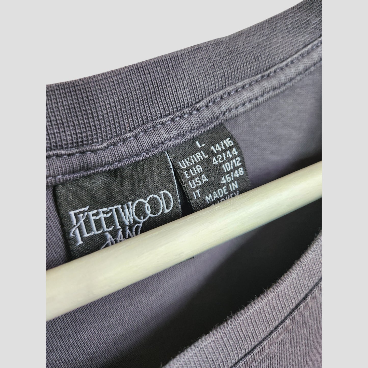 Close-up of a black Primark label inside an Upcycled Fleetwood Mac Floral Band t-shirt, size L (UK14/16), in dark grey—perfect for eco-friendly breastfeeding and pumping moms. "Made in" text is partially hidden by a hanger.