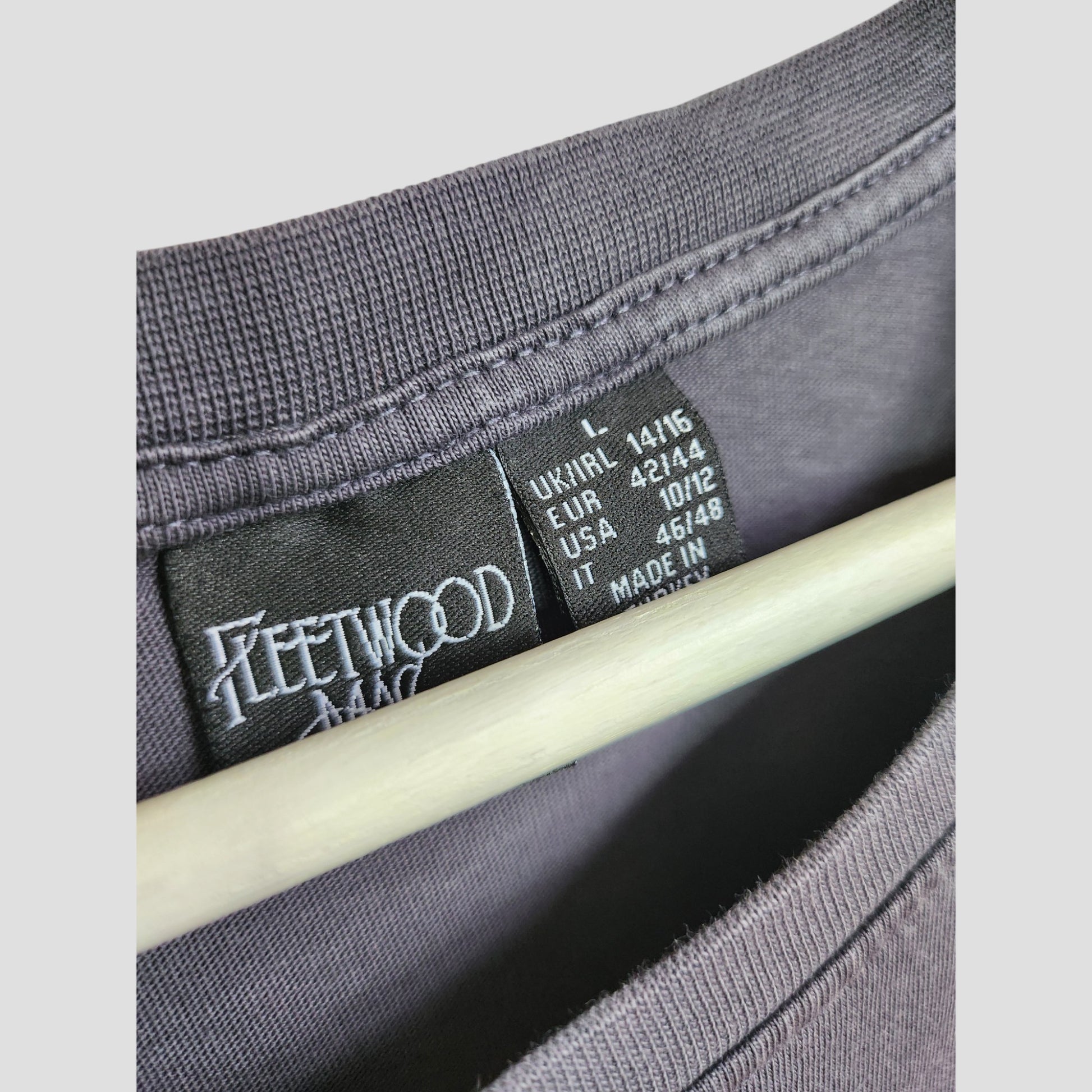 Close-up of a black Primark label inside an Upcycled Fleetwood Mac Floral Band t-shirt, size L (UK14/16), in dark grey—perfect for eco-friendly breastfeeding and pumping moms. "Made in" text is partially hidden by a hanger.