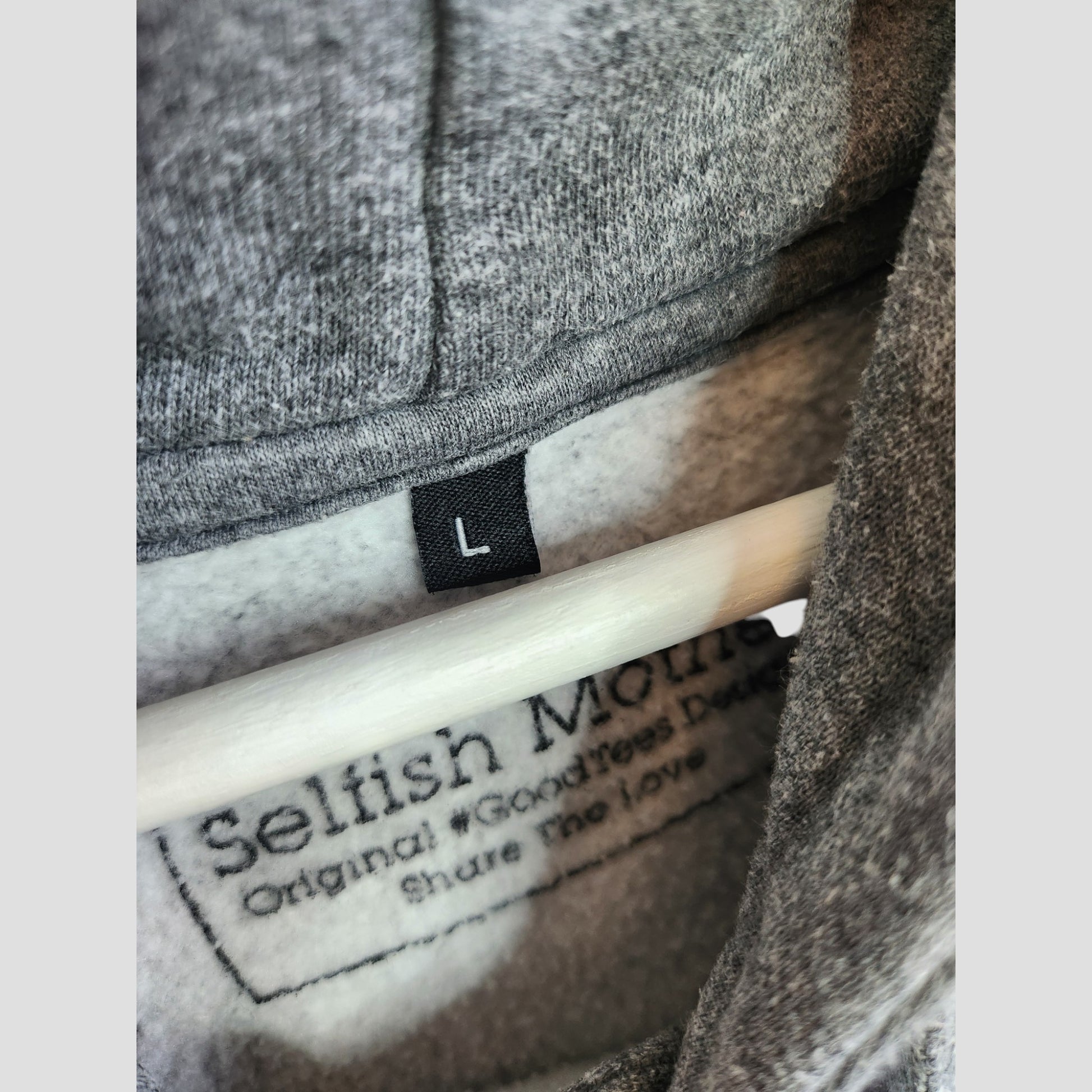 Close-up of the Selfish Mother Upcycled Breastfeeding & Pumping MAMA Hoodie L (100130) in gray fleece, hanging with a black label—an eco-friendly option for conscious moms.