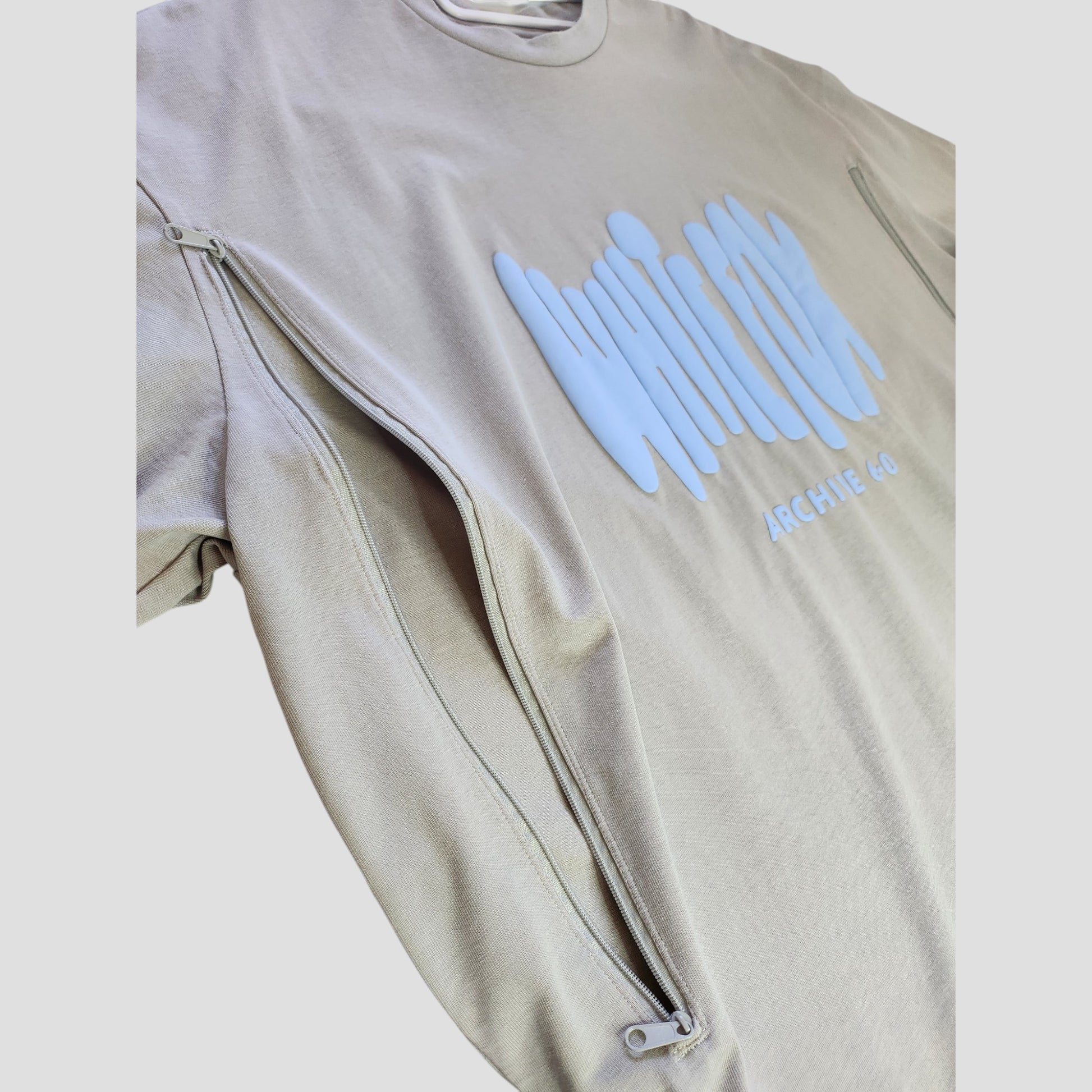 A grey/light blue White Fox t-shirt (size L) made from upcycled breastfeeding clothing, featuring a stylish abstract graphic and sleeve zippers for a unique, sustainable look.