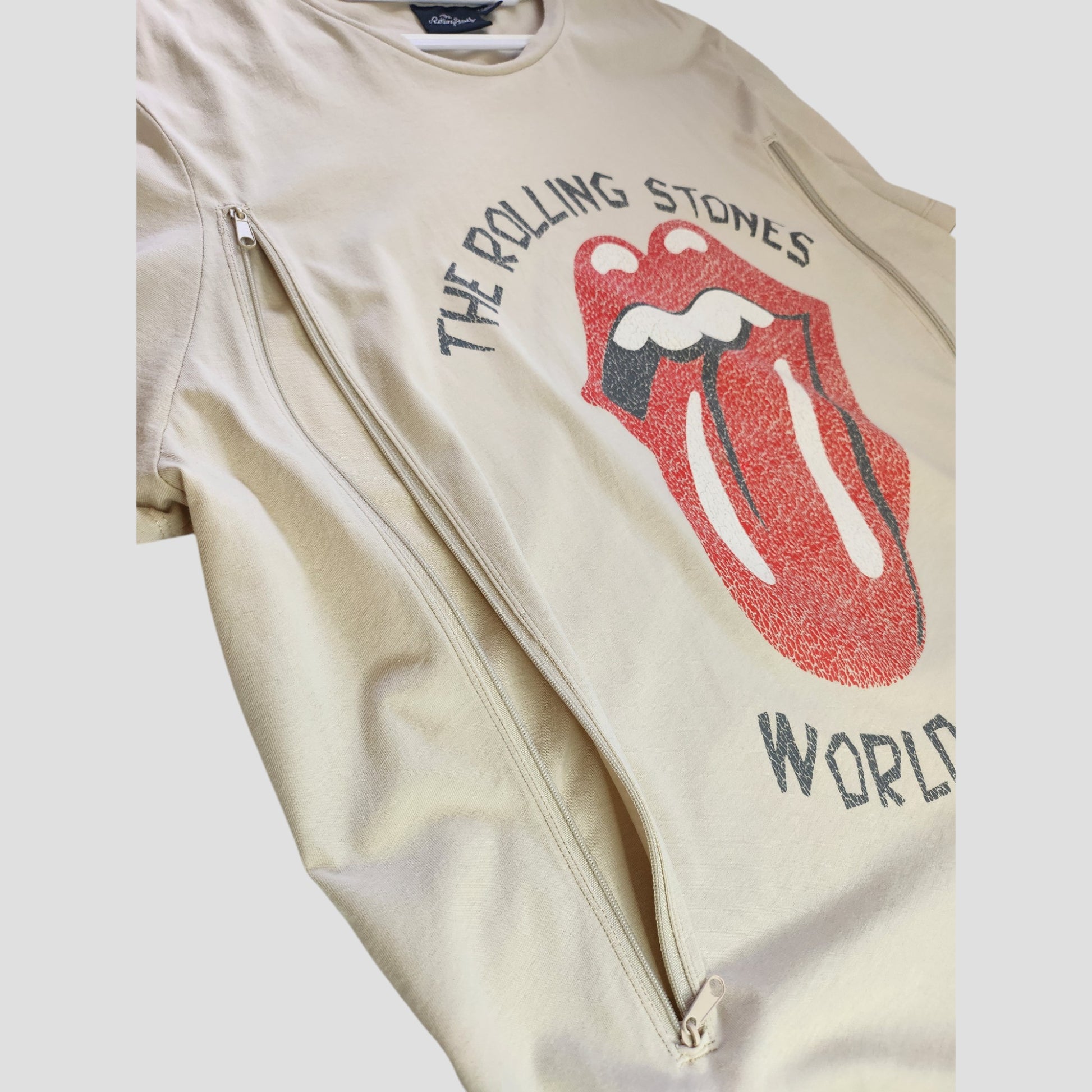 The Primark Upcycled Breastfeeding & Pumping Rolling Stones Band T-shirt (2XL) features the iconic red tongue logo, "The Rolling Stones World" print, and two diagonal zippers for easy nursing access. Color: beige/red.