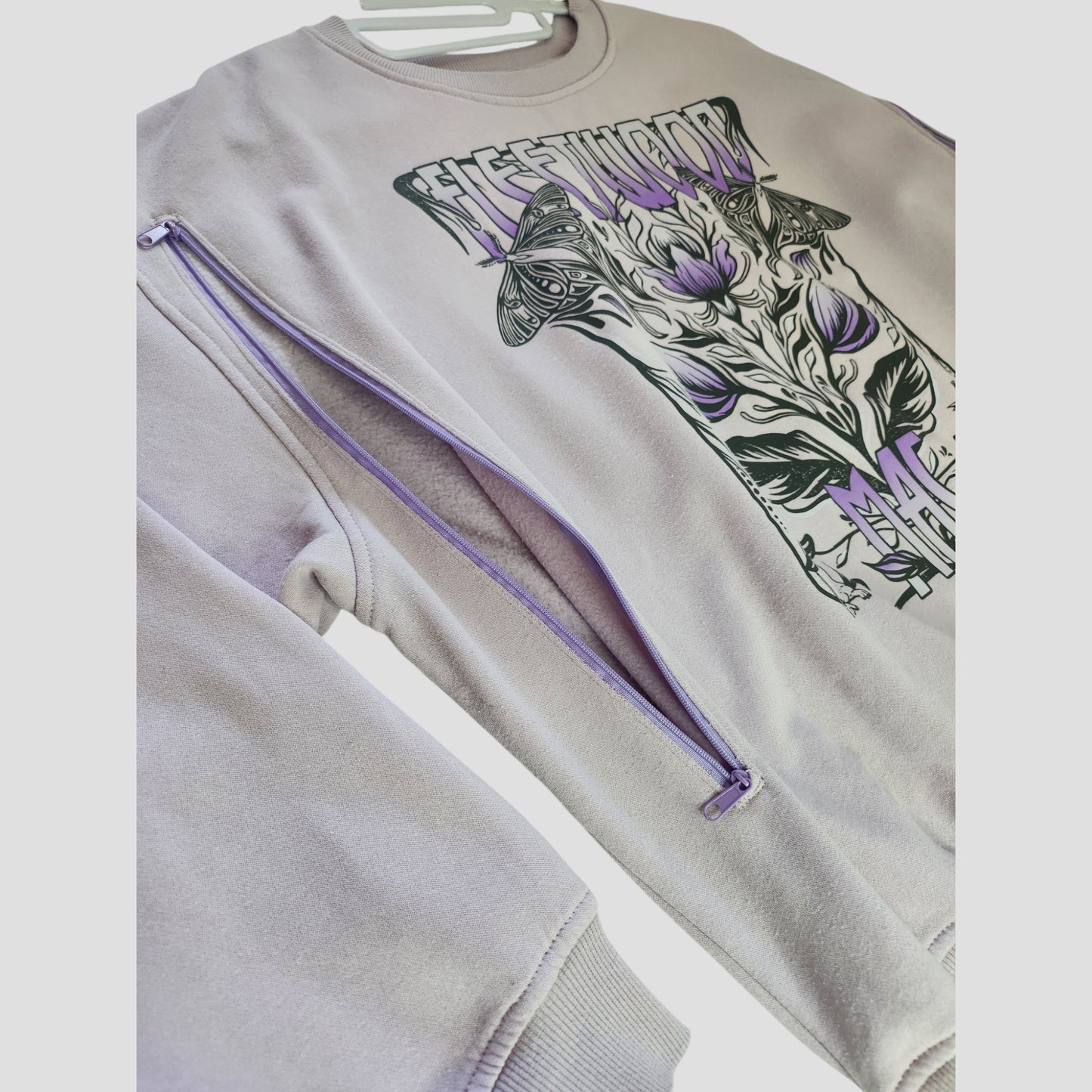 H&M Upcycled Breastfeeding & Pumping Lilac Fleetwood Mac Band Sweatshirt (XL) features sleeve zippers and a graphic of thistle flowers, butterflies, and "FLEETWOOD MAC"—a unique choice for nursing fans seeking standout style.
