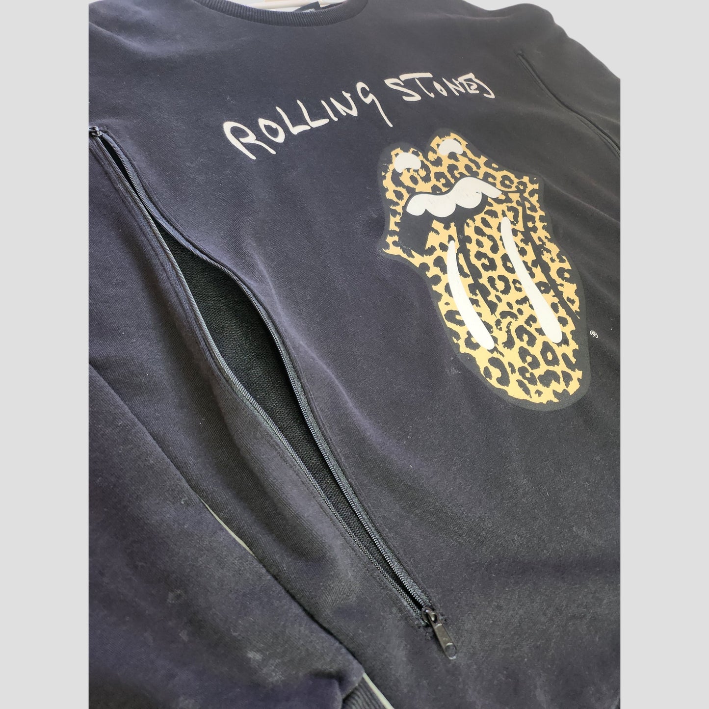 The Rolling Stones Upcycled Breastfeeding & Pumping Black/Leopard Band Sweatshirt UK14 features the iconic logo with a leopard print tongue, white text, and zippered openings—perfect for rock-loving nursing moms.