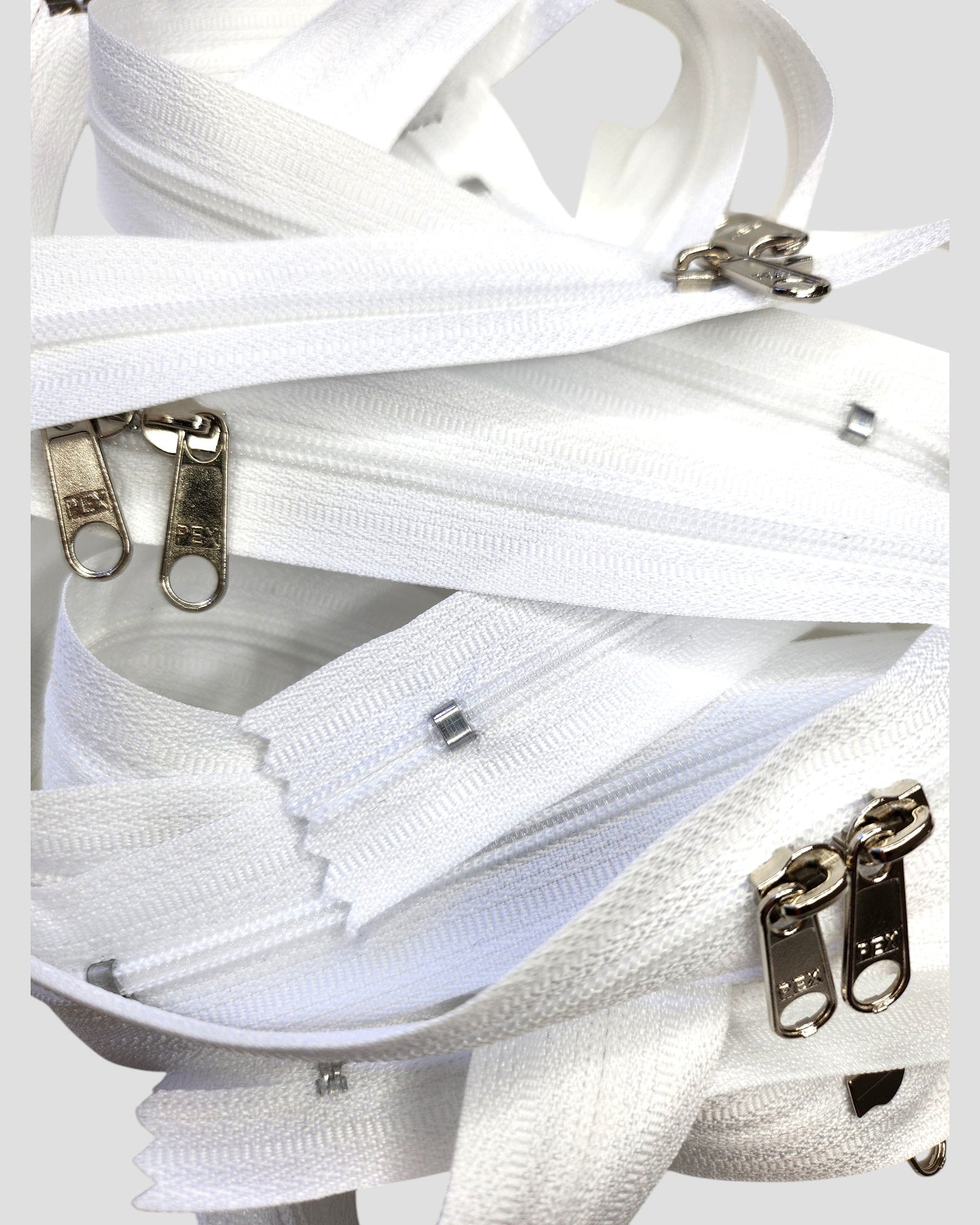 A close-up of The Original Sew-On Zip Kit by touched out mama, featuring several intertwined white zippers with silver sliders—ideal for beginner sewing or upcycling t-shirts.