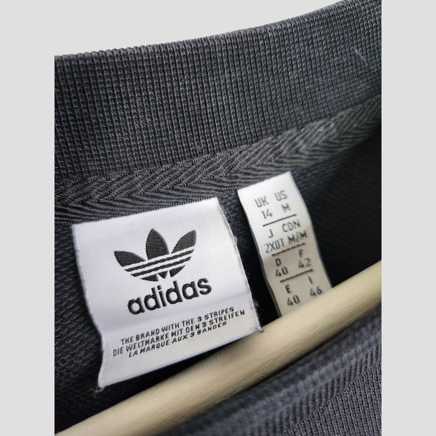 Close-up of the collar on an upcycled Adidas breastfeeding & pumping black/white sweatshirt (UK14, 100271), featuring two tags—one with Adidas branding in various languages and another with regional size info—highlighting affordable eco-friendly fashion.