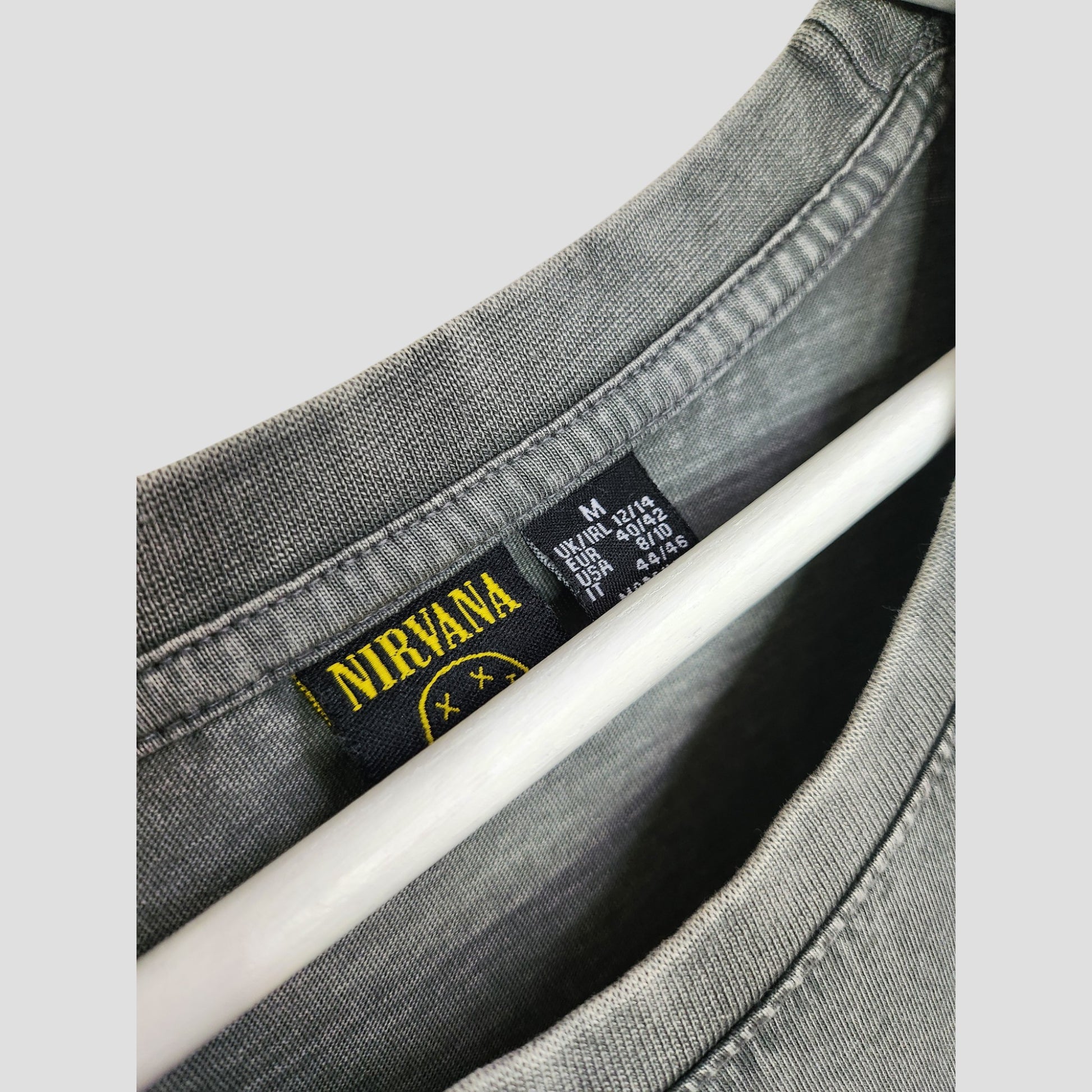 Close-up of a grey Primark Nirvana Angel oversized band t-shirt dress (M, UK12/14) for breastfeeding and pumping, featuring yellow label with smiley face logo—an eco-friendly, affordable choice upcycled from preloved clothing.
