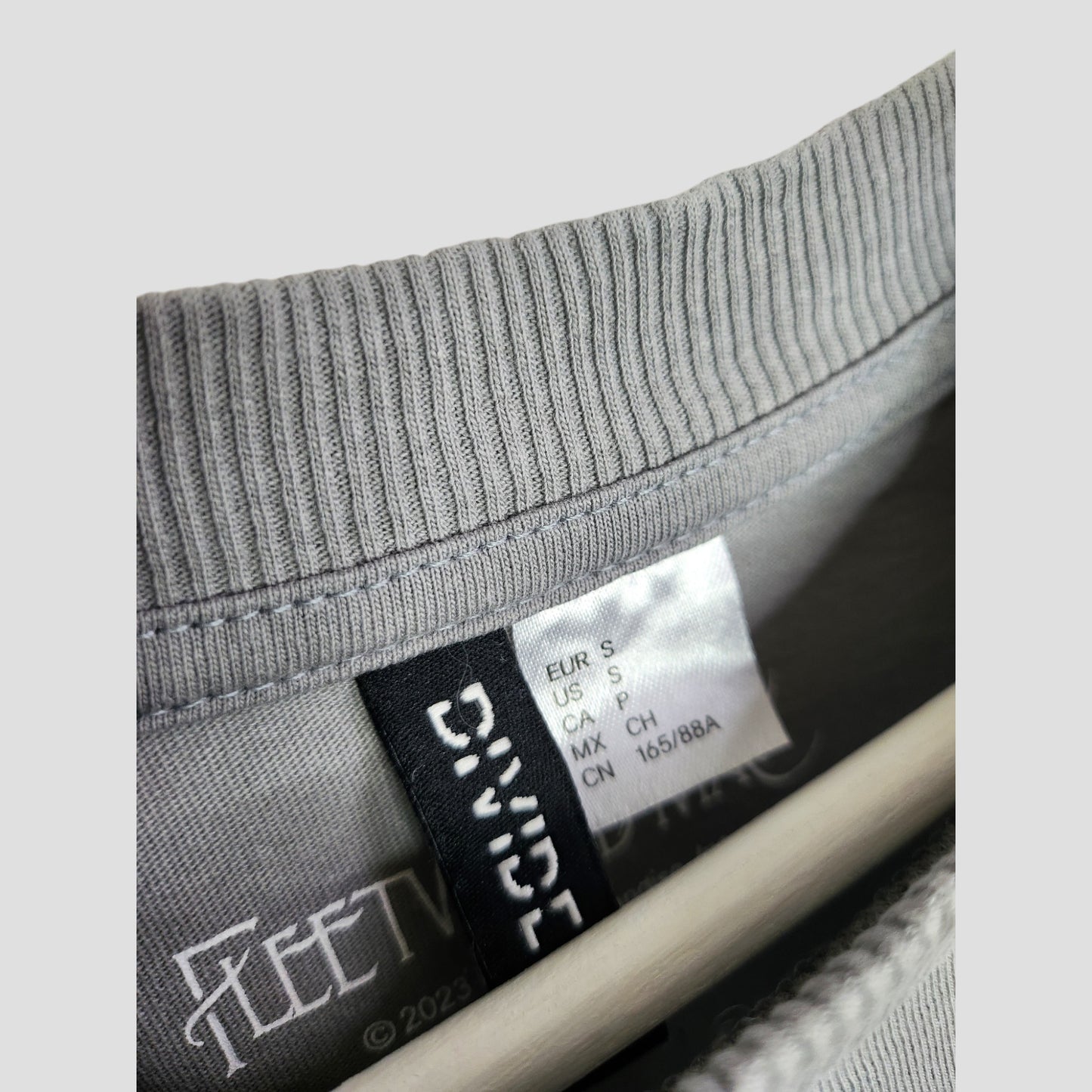 Close-up of a gray ribbed H&M sweatshirt collar with size and care tags, plus inside "FLEET" logo. Displayed on a hanger—this upcycled Fleetwood Mac Dreams S band t-shirt is ideal eco-friendly nursing and pumping wear.