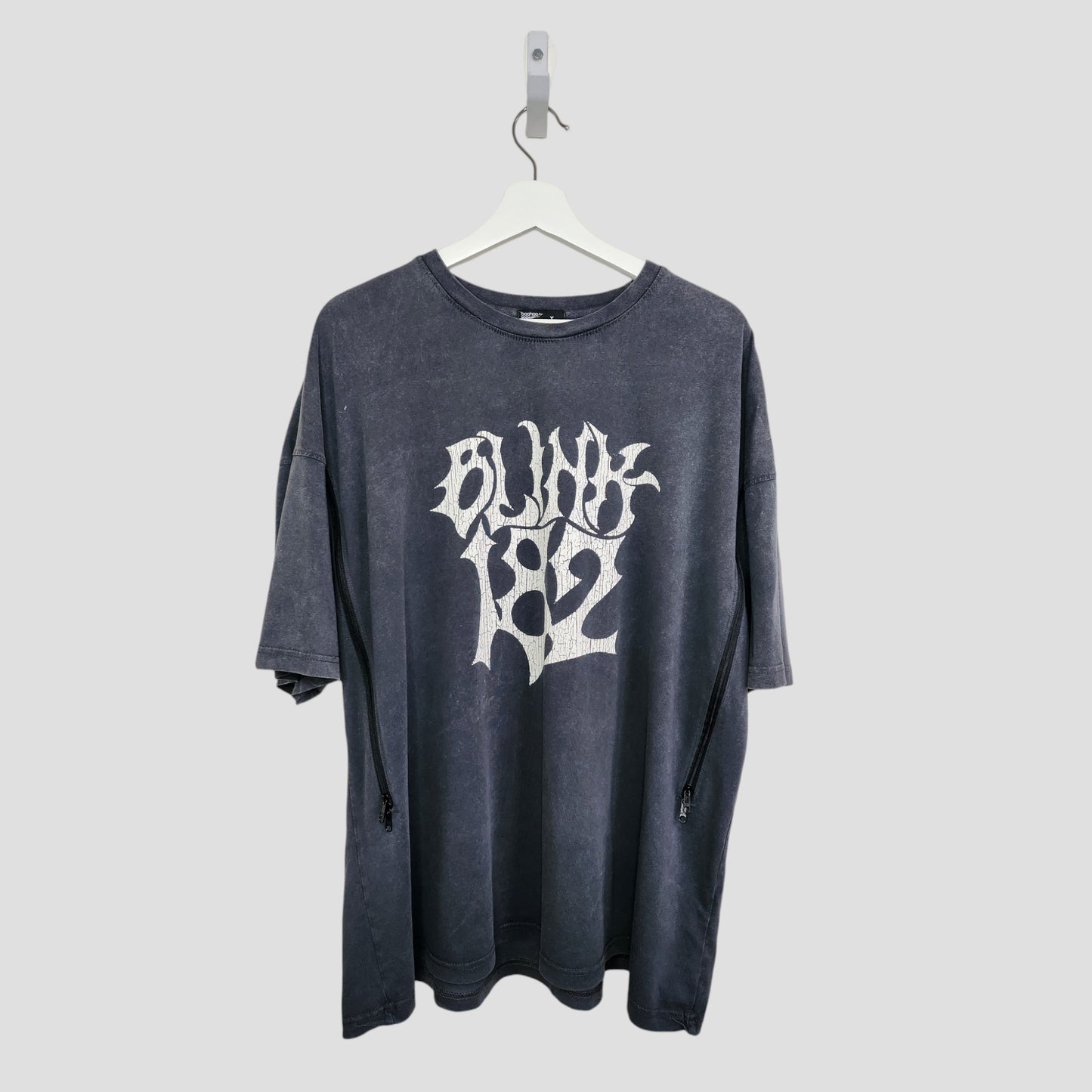 The Boohoo Upcycled Breastfeeding & Pumping Blink 182 Band T-shirt (M, 100324) is a black oversized tee with bold white BLINK 182 text on the front, made from repurposed nursing wear and shown hanging on a white hanger against a light gray background.