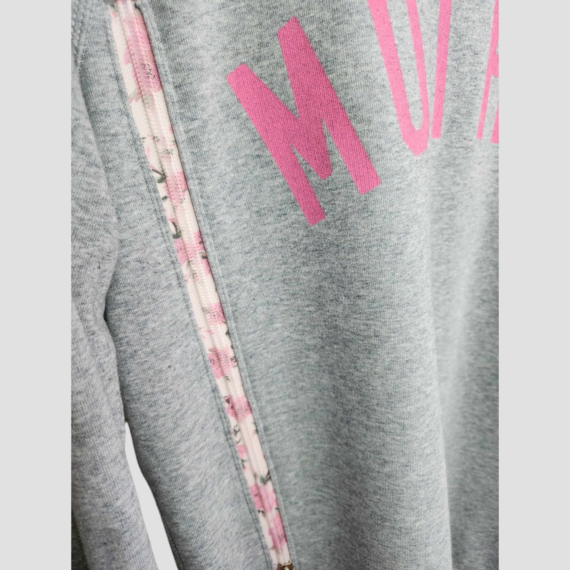 Close-up of the Selfish Mother Upcycled Breastfeeding & Pumping Grey/Pink MOTHER Sweatshirt (L), featuring pink printed letters and a decorative zipper with a pink and white floral pattern along the shoulder seam.