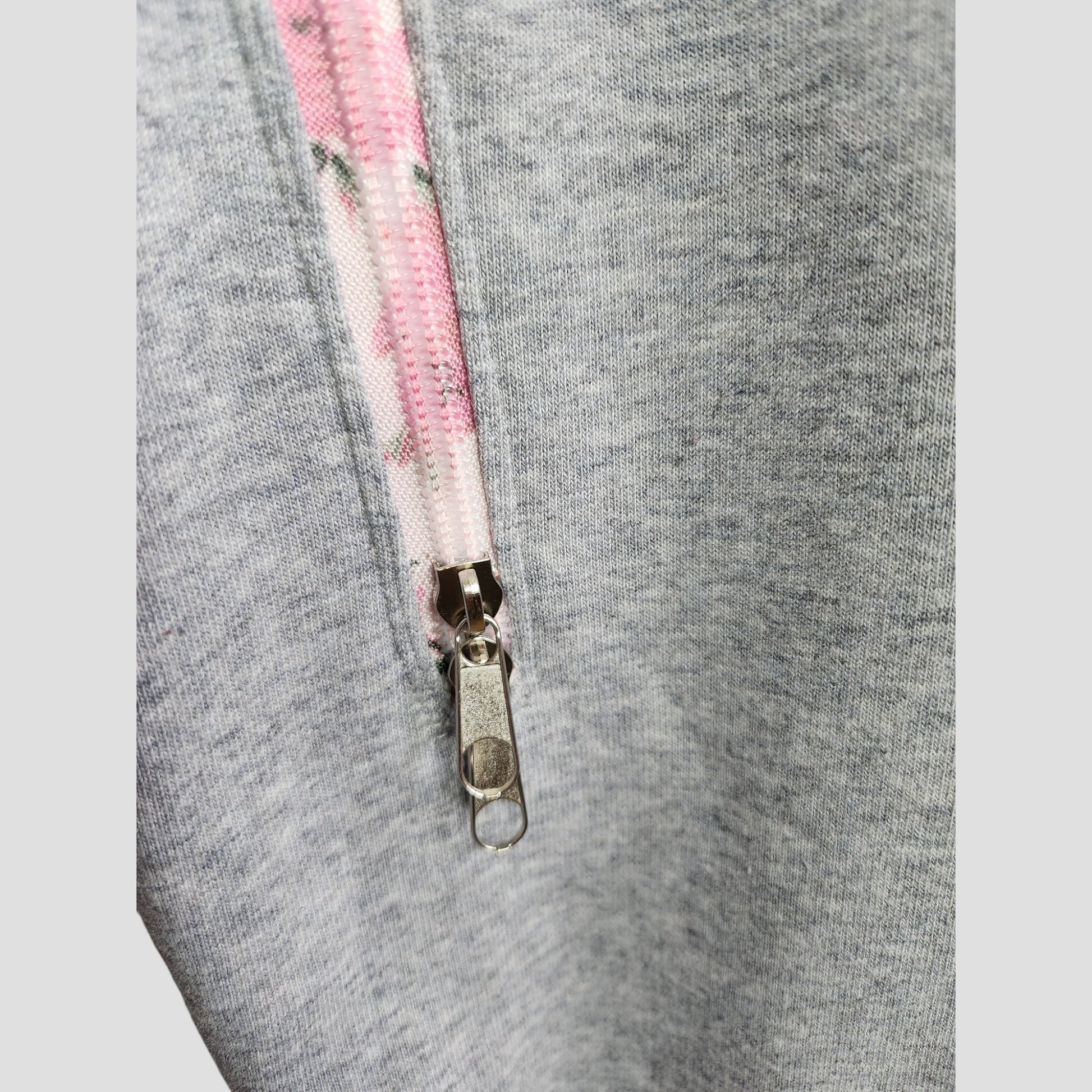 Close-up of the Selfish Mother Upcycled Breastfeeding & Pumping Grey/Pink MOTHER Sweatshirt L, showing a silver zipper on light grey fabric with white tape featuring a pink floral pattern for a stylish, eco-friendly touch.