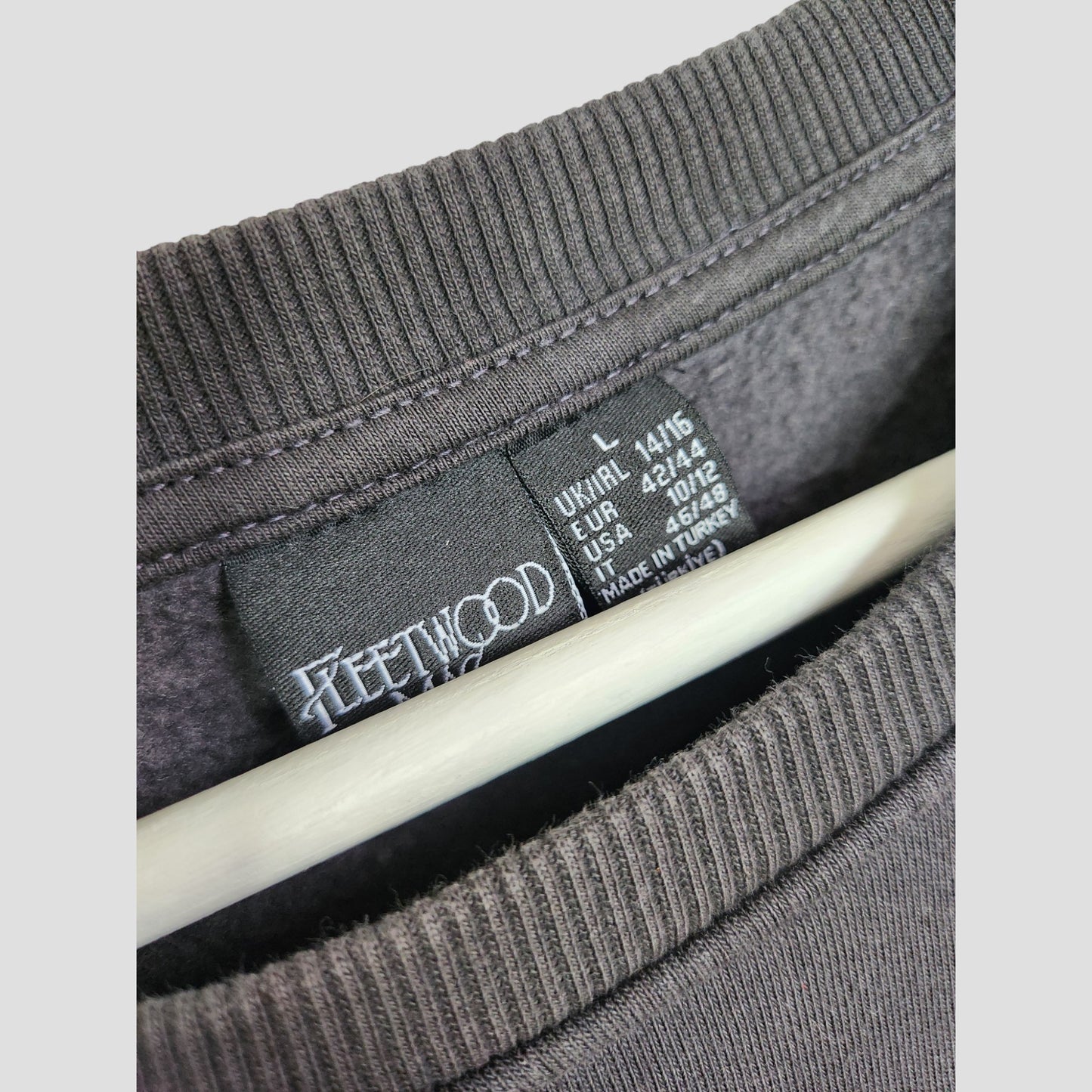 Close-up of a grey Upcycled Breastfeeding & Pumping Floral Fleetwood Mac Band Sweatshirt by Primark, size L (UK14/16), shows the neckline label and care info. Eco-friendly nursing garment with partial hanger visible.