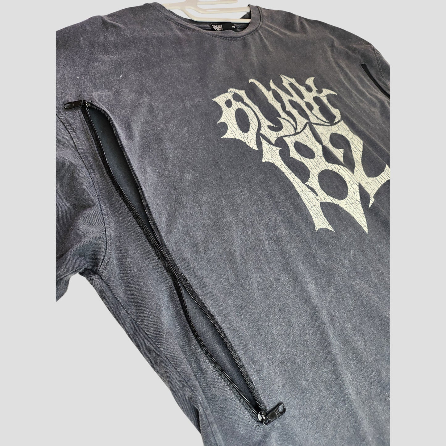 The Boohoo Upcycled Breastfeeding & Pumping Blink 182 Band t-shirt (M) features a black long-sleeve design with a white graphic and diagonal zipper—an eco-friendly nursing top crafted from upcycled materials.