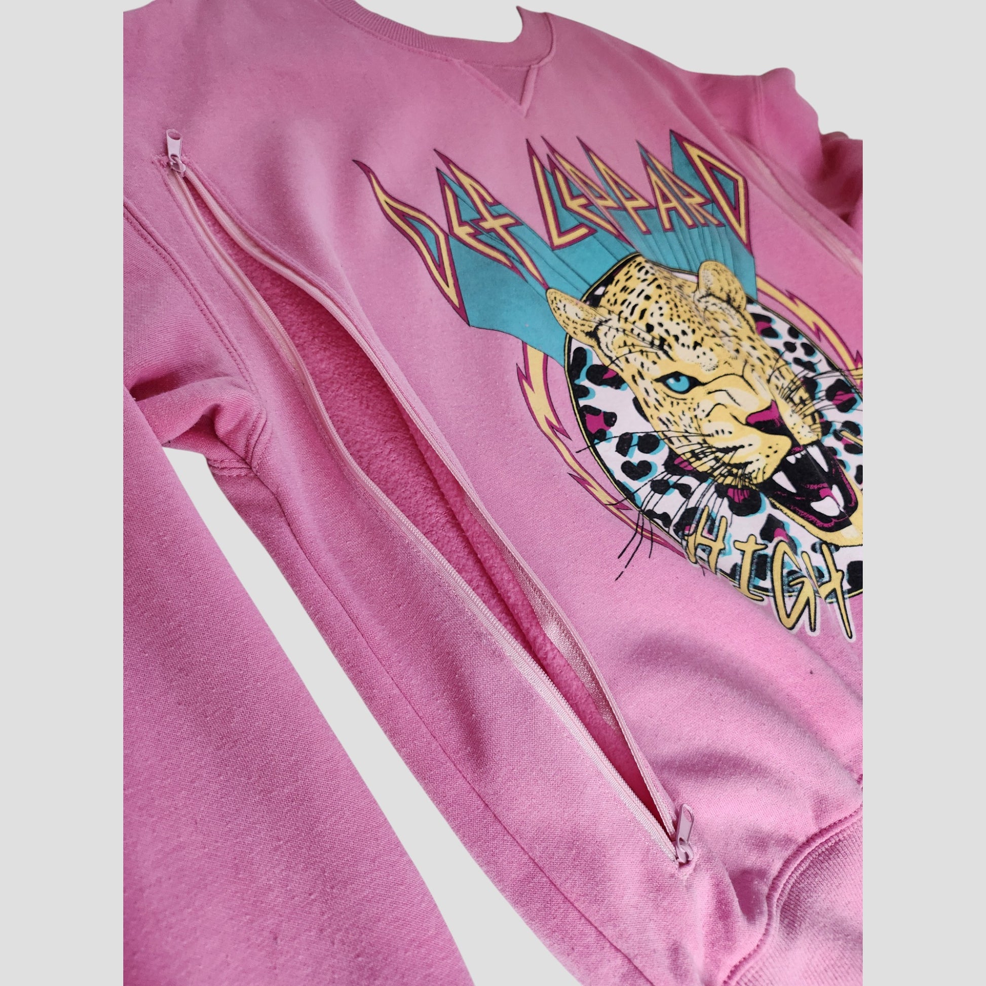 The H&M Upcycled Breastfeeding & Pumping Pink Def Leppard Band Sweatshirt (M, 100131) features side zippers for nursing, a graphic leopard, and bold band text—ideal for stylish, eco-conscious moms.