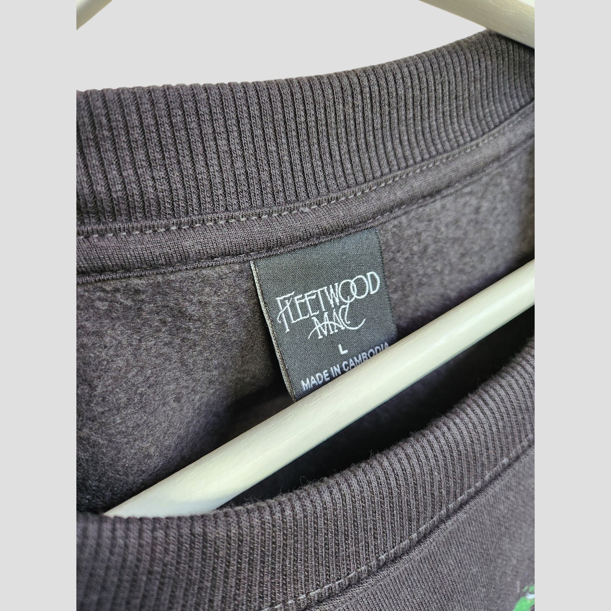 A close-up of a black Primark Upcycled Breastfeeding & Pumping Embroidered Fleetwood Mac Band Oversized Sweatshirt L shows its label. Made from upcycled clothing, the soft fabric offers an affordable, eco-friendly choice and hangs neatly on a hanger.
