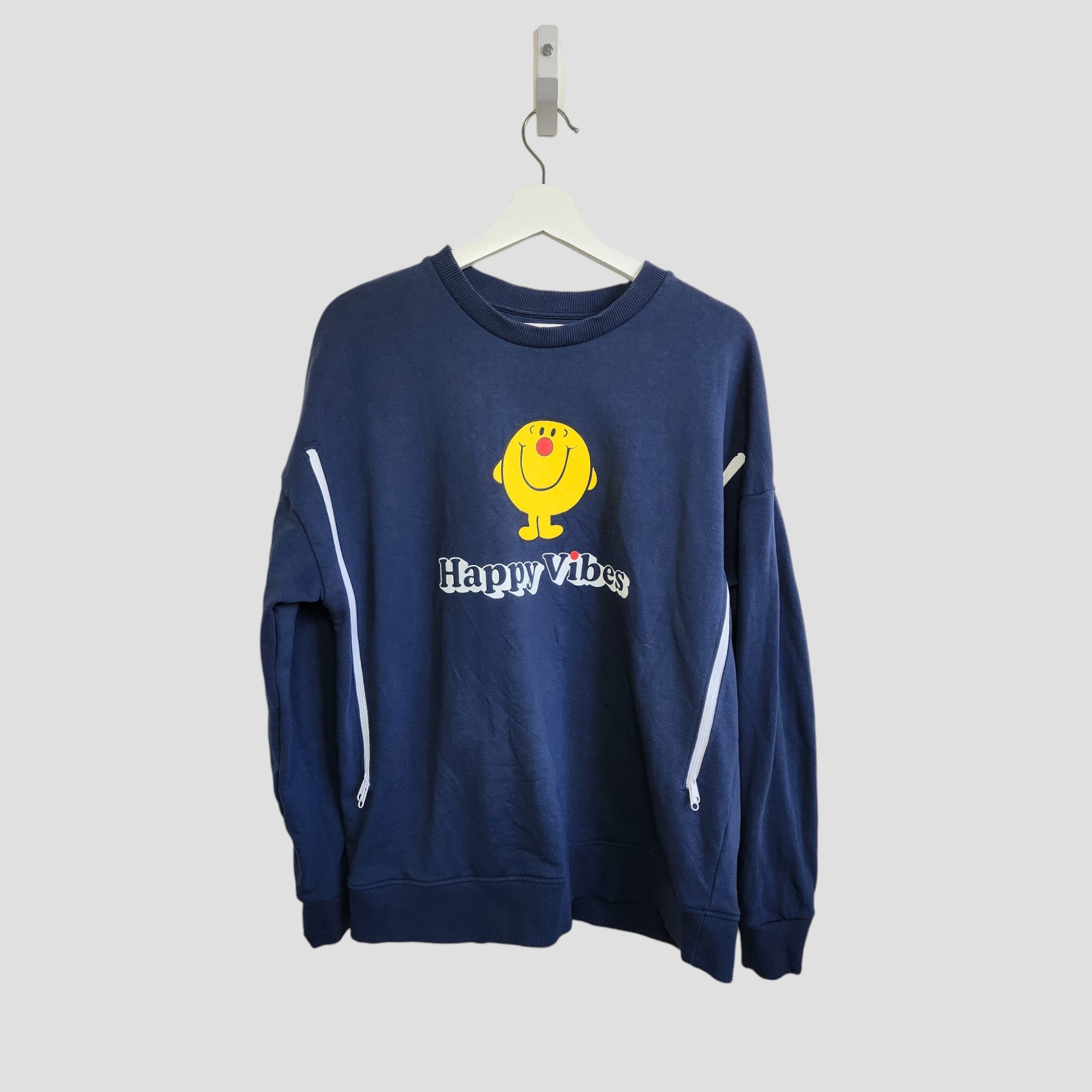 The Comic Relief Upcycled Breastfeeding & Pumping Happy Vibes Sweatshirt (L) features a yellow smiling face and text on navy blue fabric, crafted from eco-friendly materials, and is displayed on a white hanger against a light gray background.