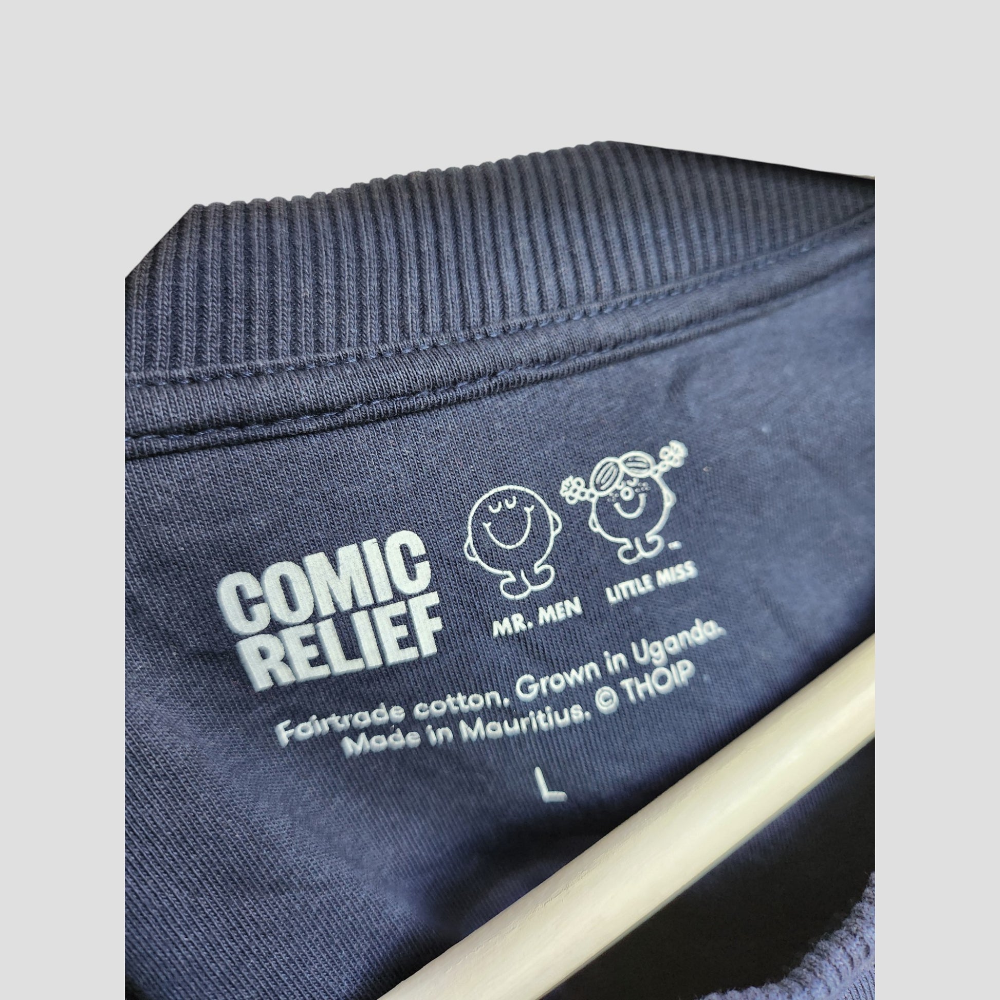 Close-up of the navy label on Upcycled Breastfeeding & Pumping Happy Vibes Sweatshirt L by Comic Relief, featuring Mr. Men and Little Miss, “Fairtrade cotton, Grown in Uganda. Made in Mauritius. © THOIP,” and size L details.