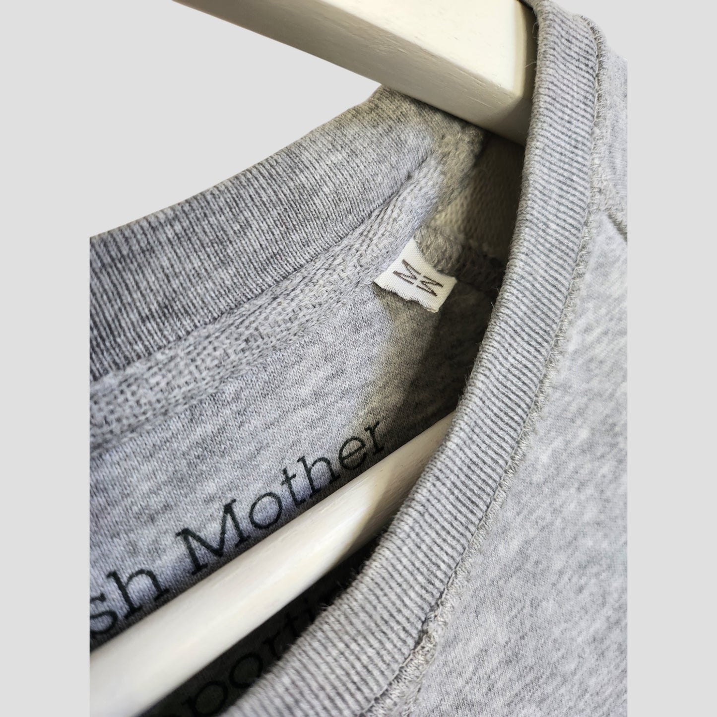 Close-up of two Selfish Mother grey Upcycled Breastfeeding & Pumping "WINGING IT" Sweatshirts (M) on hangers, showing the collar, white size tag (M), and “Mother” text inside—highlighting this stylish, upcycled nursing wear.