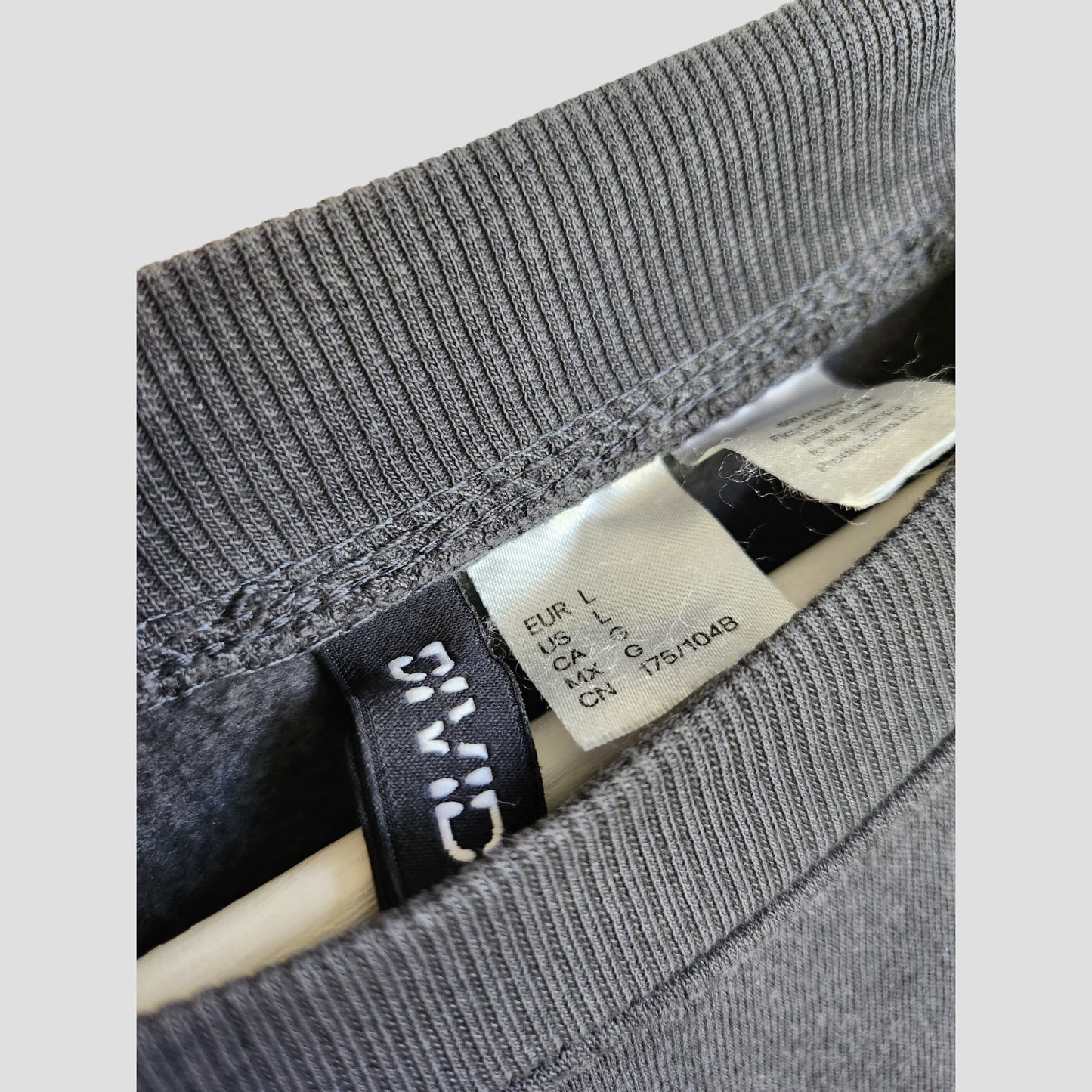 Close-up of an H&M Upcycled Breastfeeding & Pumping Pink Floyd Band Oversized Sweatshirt collar, showing inside tags with size info and care instructions—perfect for eco-conscious nursing wear seekers. Size L (100176). Wooden hanger partly visible.