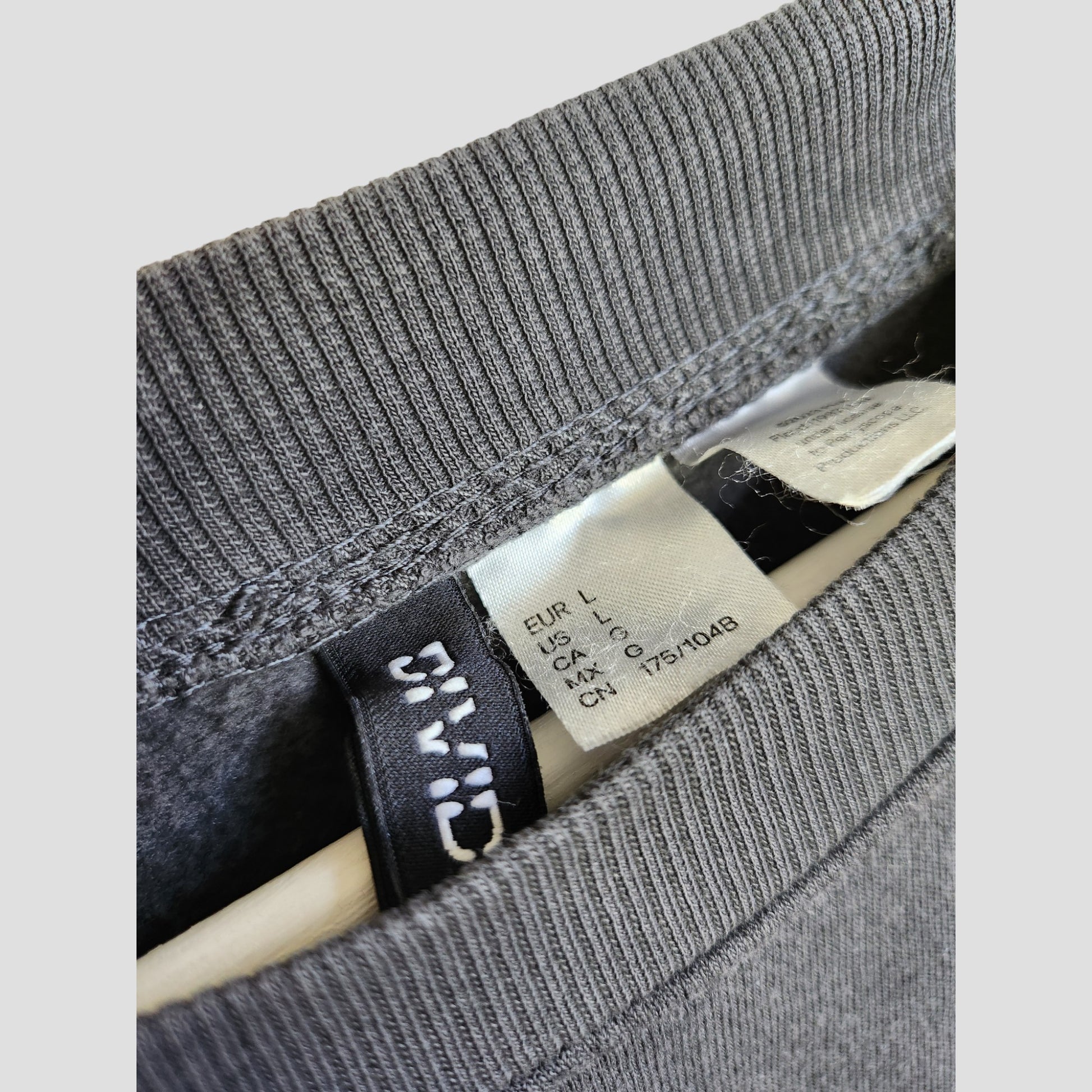 Close-up of an H&M Upcycled Breastfeeding & Pumping Pink Floyd Band Oversized Sweatshirt collar, showing inside tags with size info and care instructions—perfect for eco-conscious nursing wear seekers. Size L (100176). Wooden hanger partly visible.